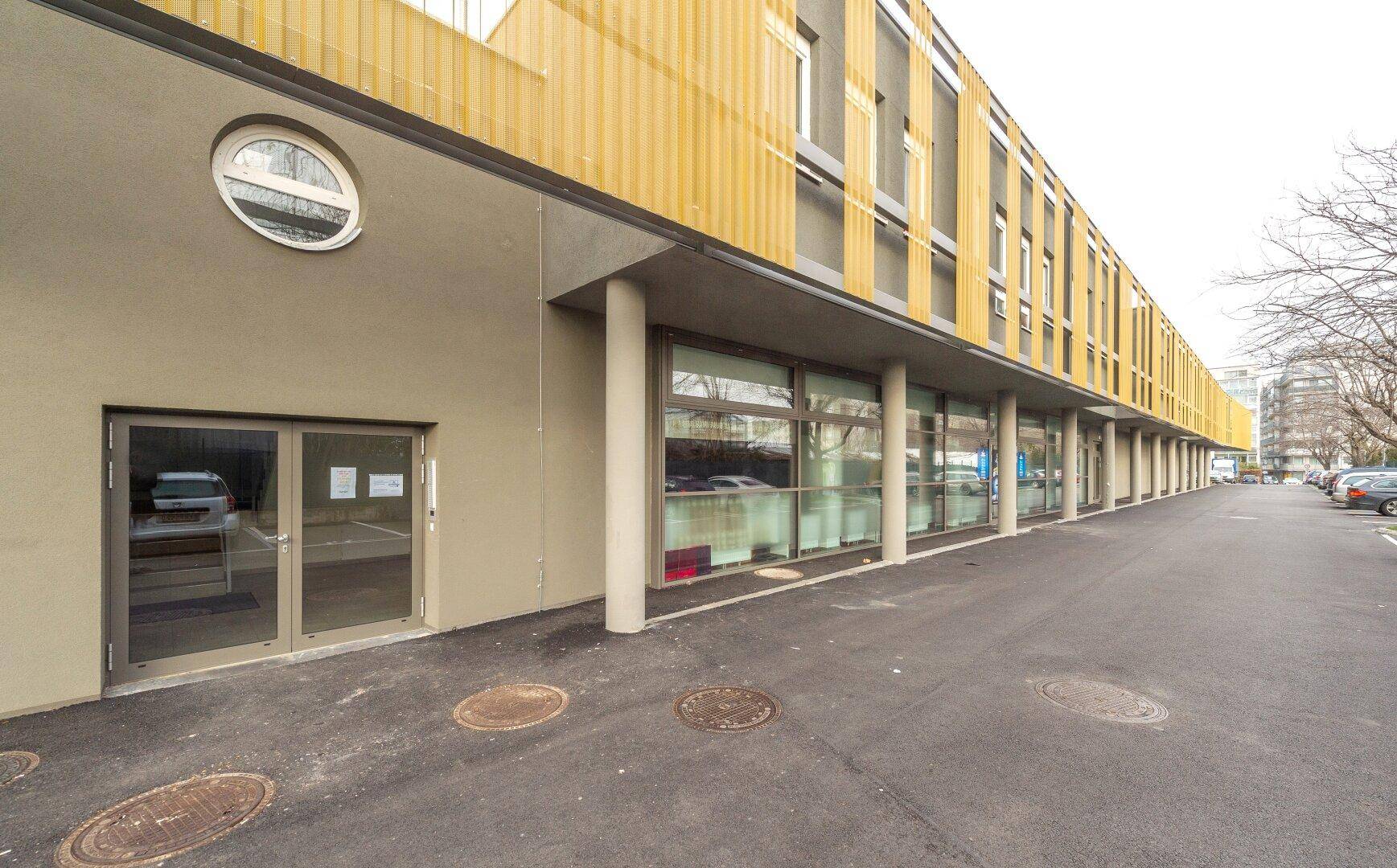 Moderne Geschäftsfassade mit gelben Akzenten und großen Schaufenstern entlang eines Parkplatzes.