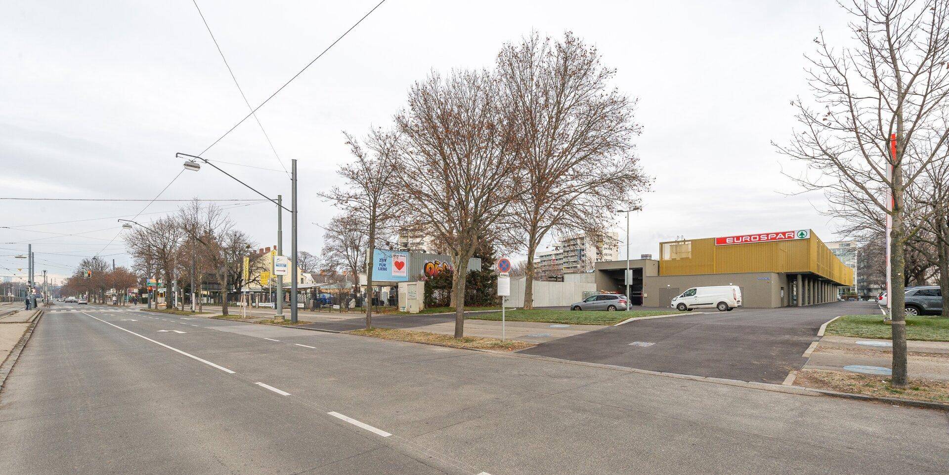 Straßenansicht mit dem Eurospar-Gebäude in der Ferne, umgeben von Bäumen und städtischer Infrastruktur.
