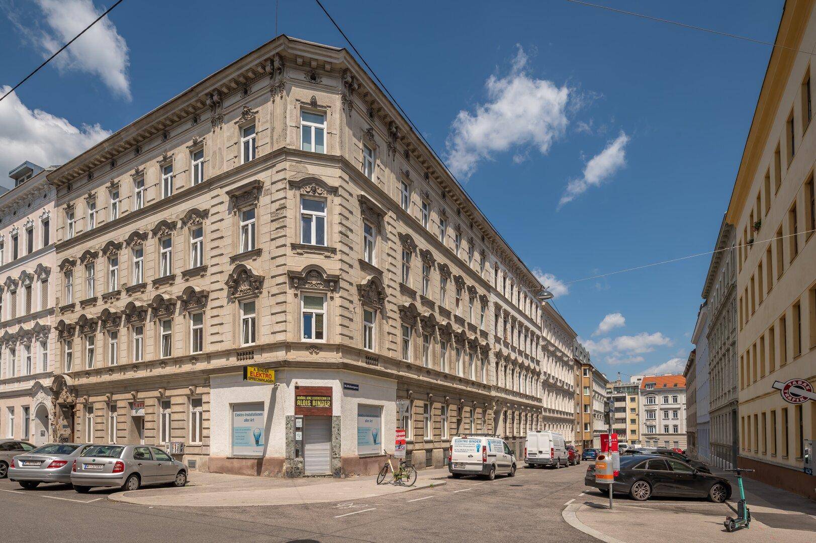 Elegantes Eckgebäude mit klassischer Architektur und vielen Fenstern in einer städtischen Umgebung.