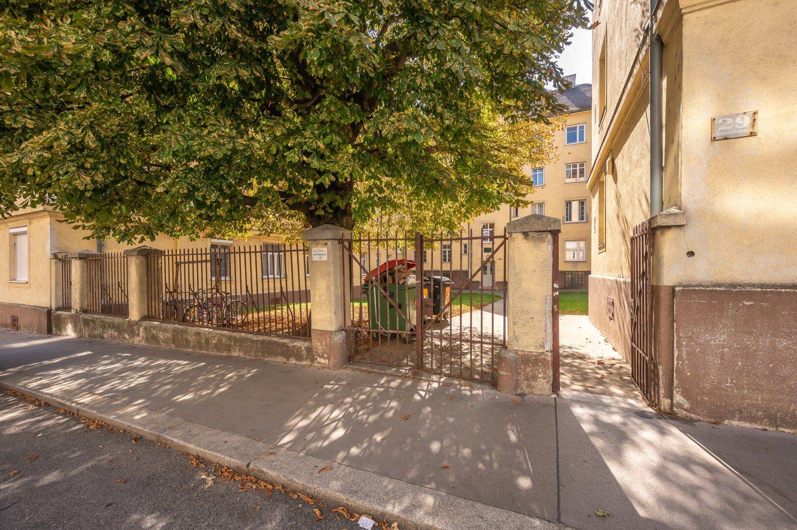 Eingangsbereich eines Wohngebäudes mit Zaun und Mülltonnen an der Straße.