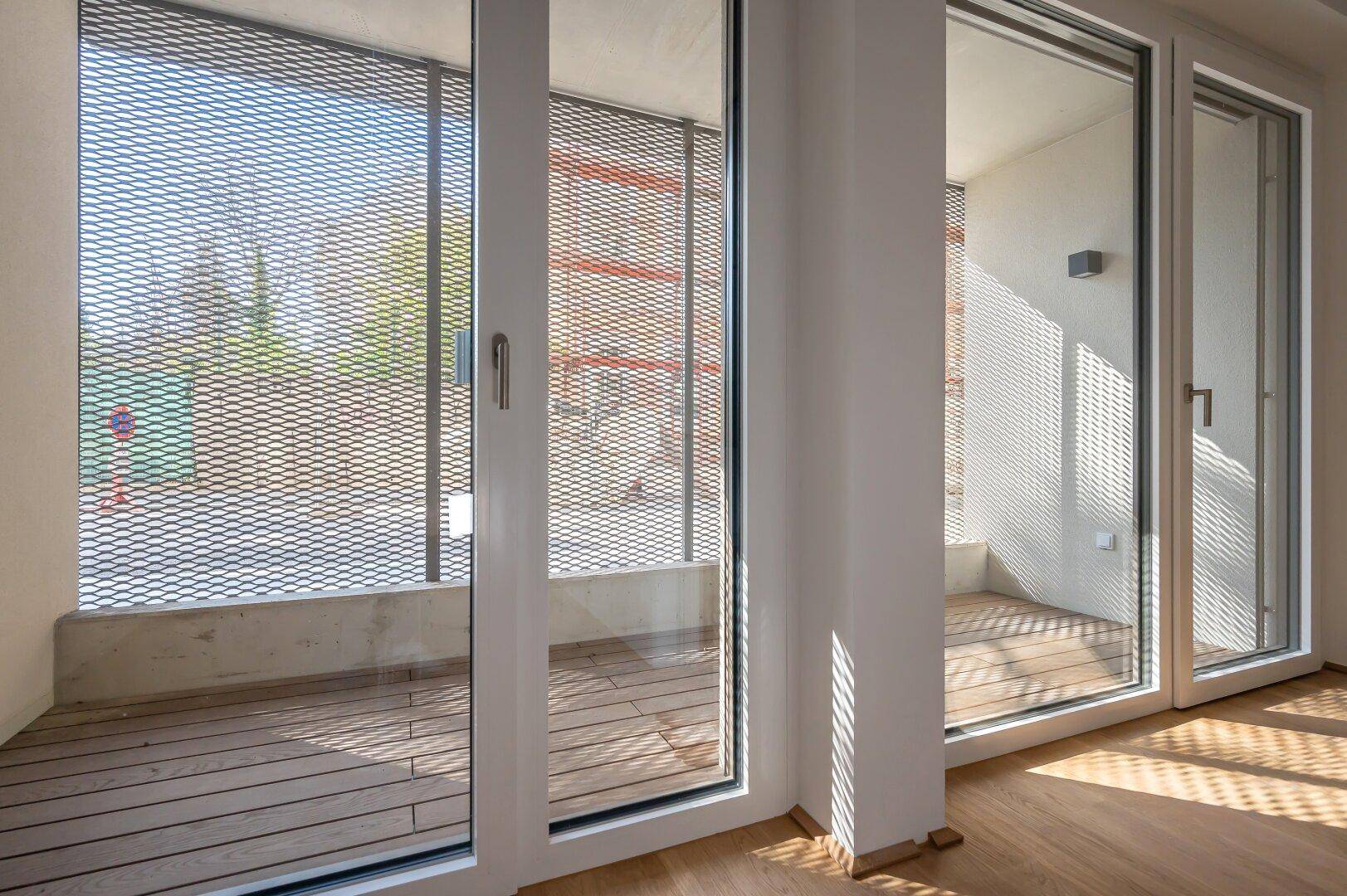 Innenraum mit Holzboden und großzügigem Zugang zu einem Balkon mit Metallgitter-Brüstung.