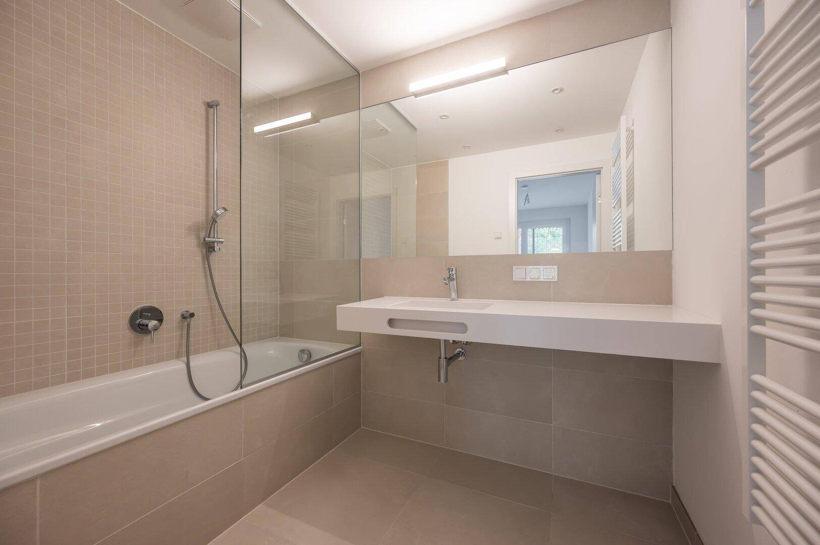 Modernes Badezimmer mit Badewanne, Duschwand und großem Spiegel über dem Waschbecken.
