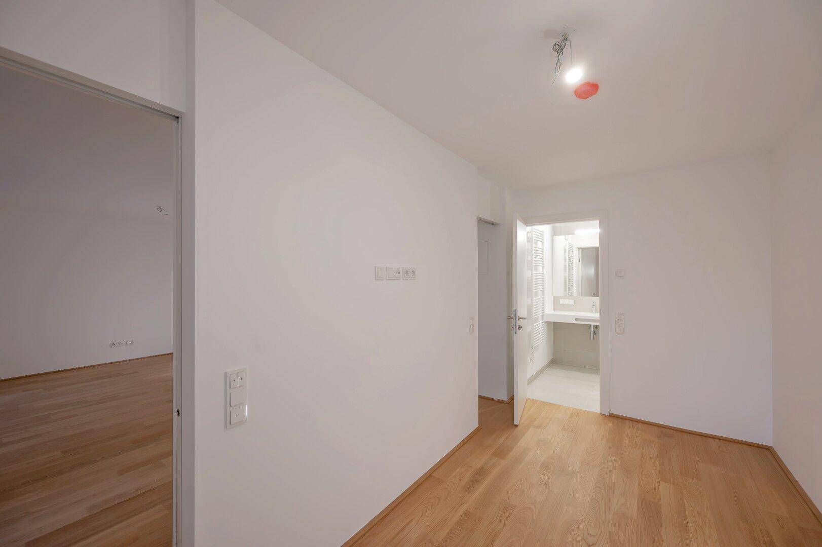 Heller Raum mit Parkettboden und einer Tür, die zu einem Badezimmer führt, ideal für Schlafzimmer oder Büro.