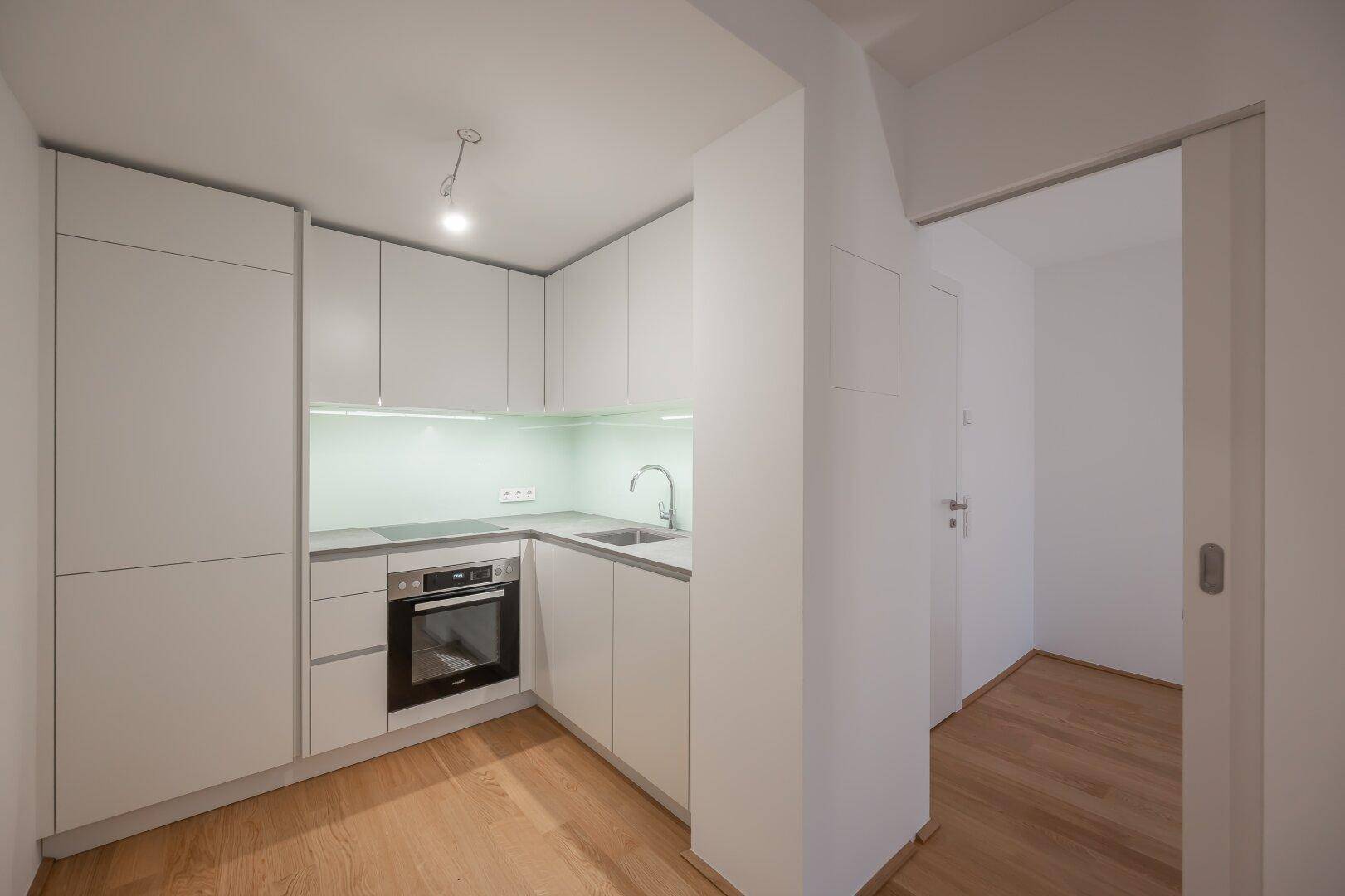 Moderne, kompakte Einbauküche mit weißen Schränken, integriertem Backofen und Spüle.
