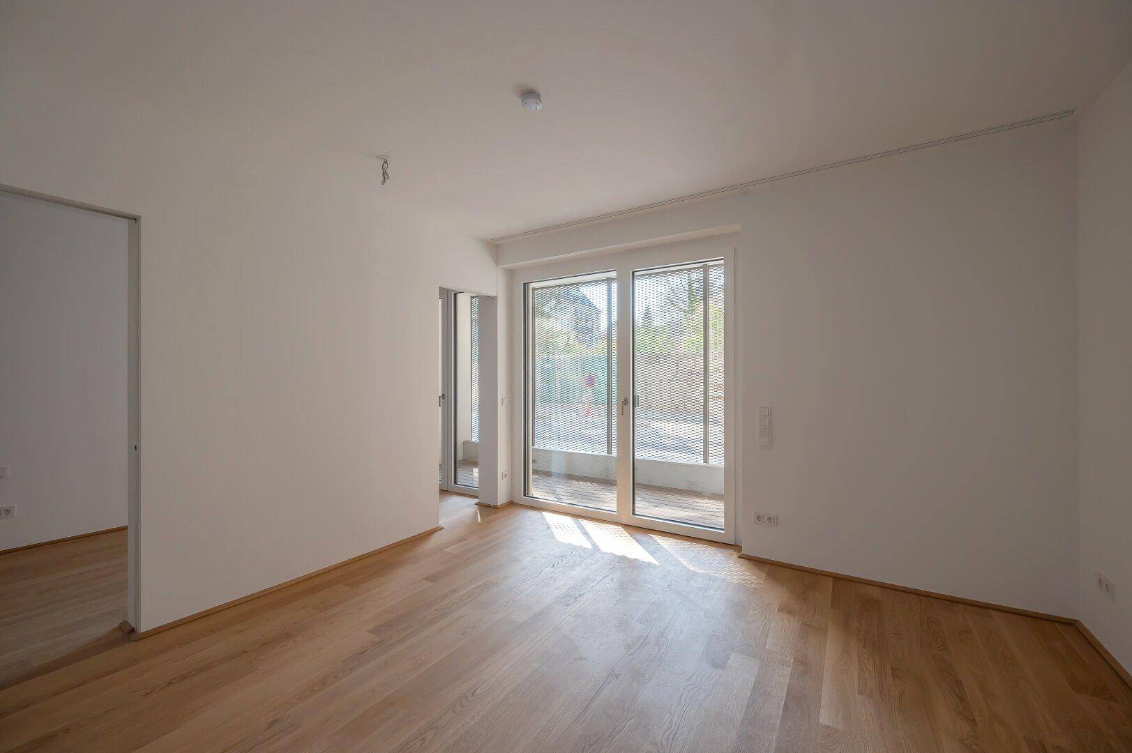 Heller Wohnbereich mit Parkettboden und großzügigem Zugang zu einem Balkon, ideal für Entspannung.