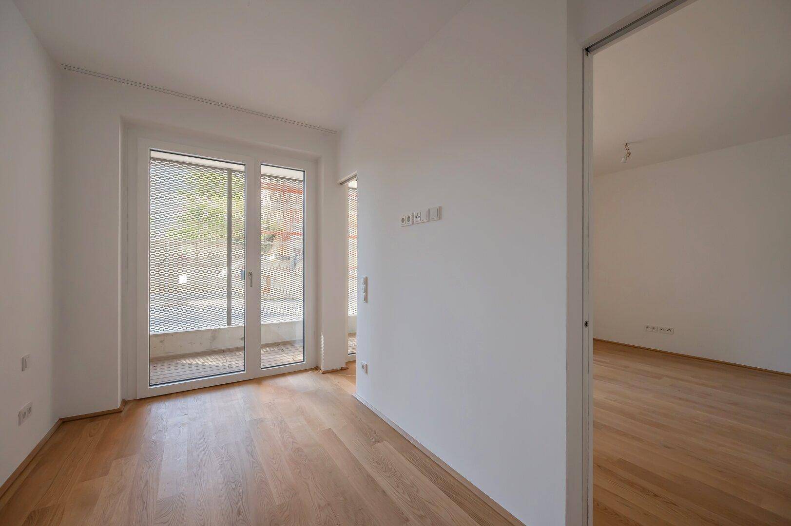Helles Schlafzimmer mit Parkettboden und direktem Zugang zu einem Balkon, bietet viel Tageslicht.