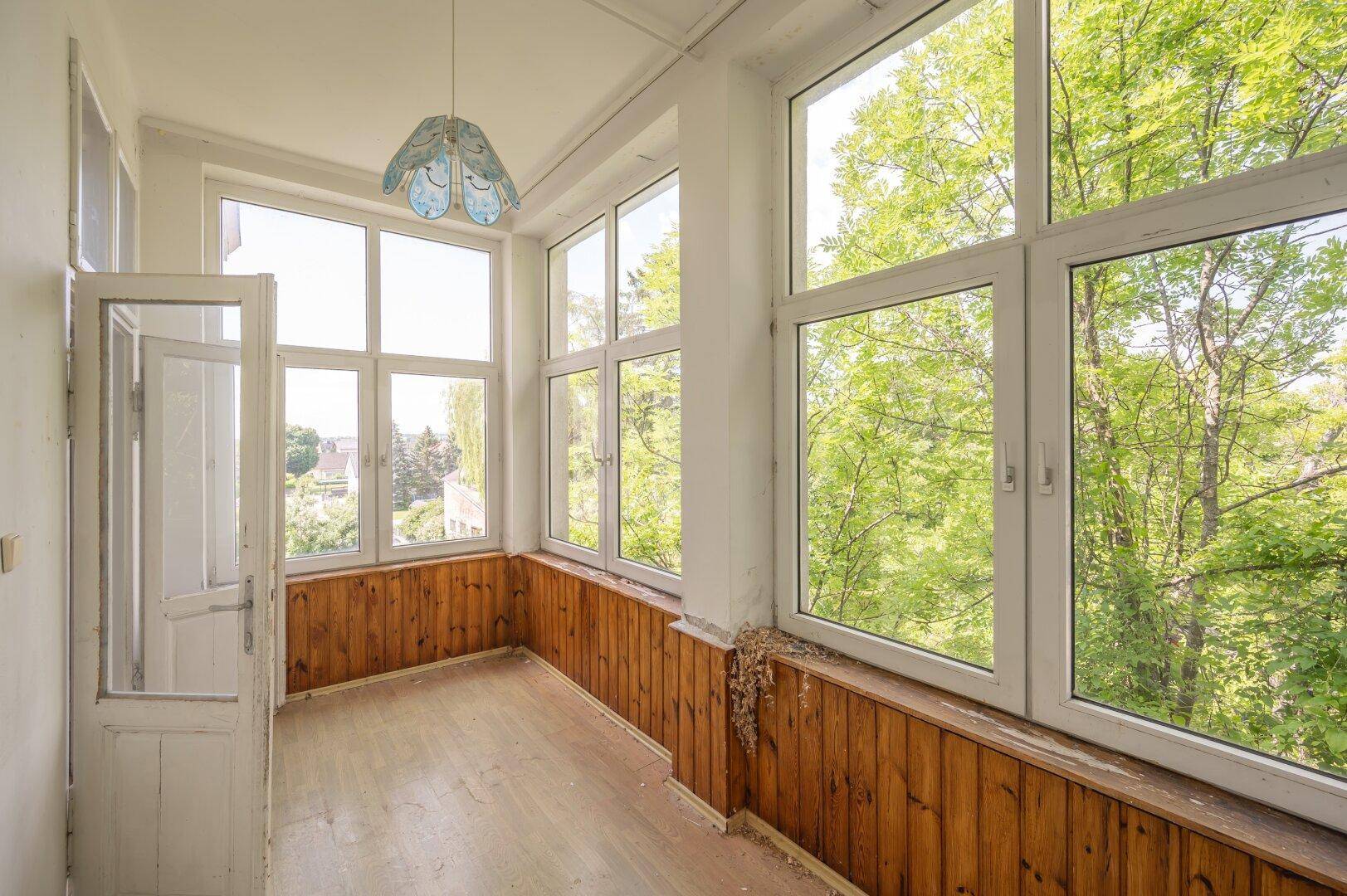 Heller Wintergarten mit Holzverkleidung und vielen Fenstern, die viel Tageslicht hereinlassen.