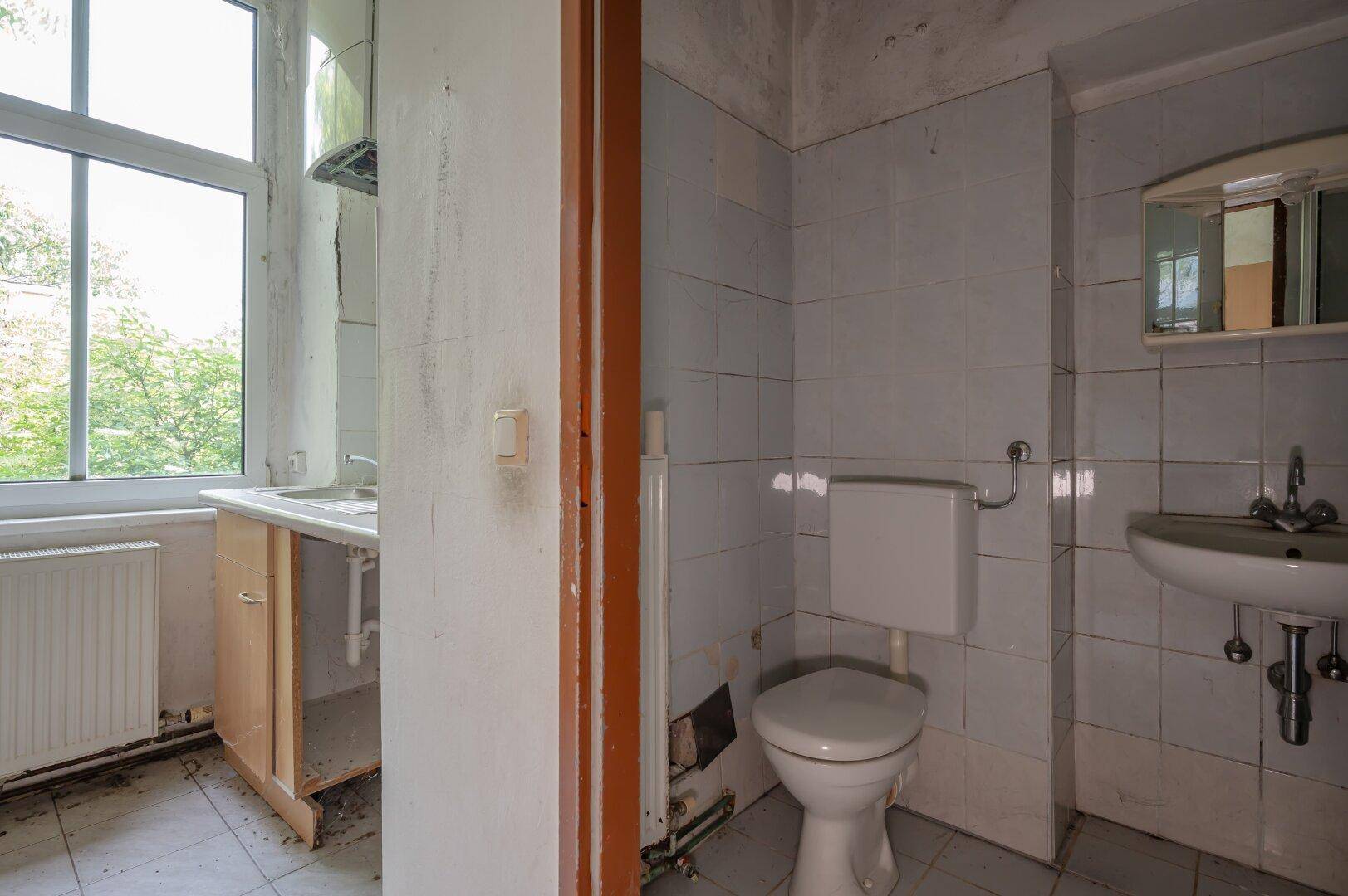 Kleines WC mit Fenster, Toilette und Waschbecken, das eine Modernisierung erfordert.