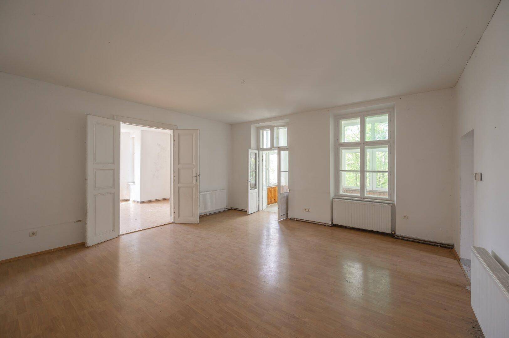 Großes, helles Zimmer mit Laminatboden und Doppeltüren, ideal für einen offenen Wohnbereich.