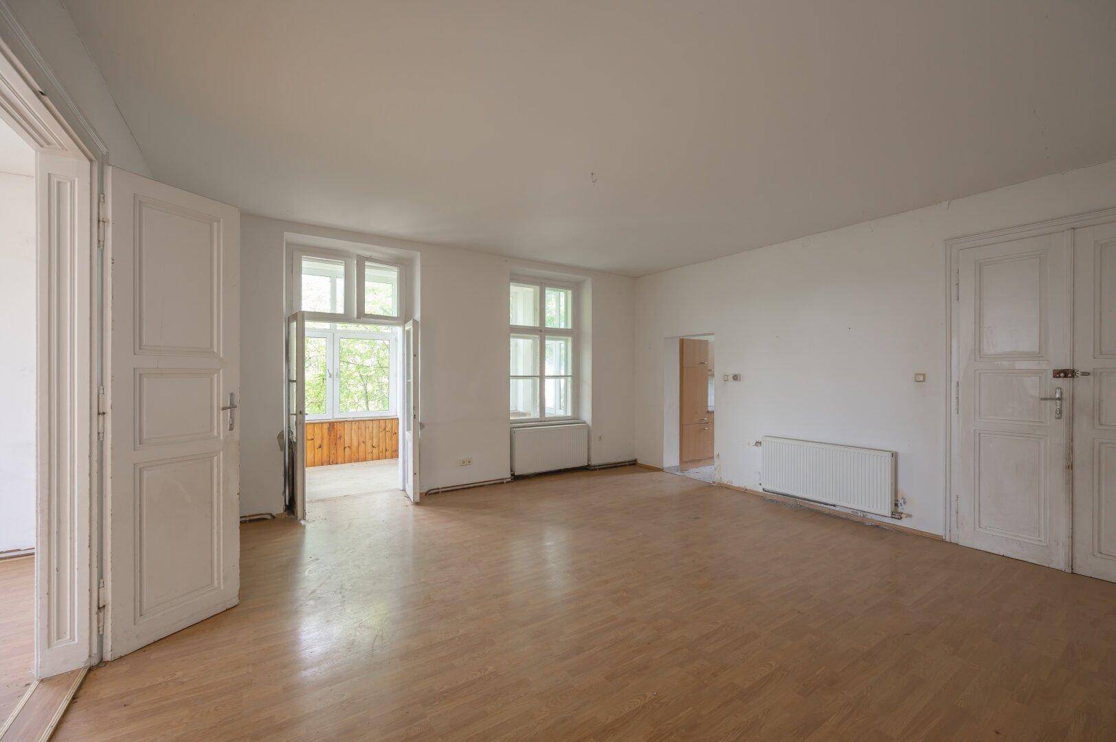Geräumiges Zimmer mit Laminatboden und Zugang zu einem verglasten Wintergarten, viel Tageslicht.