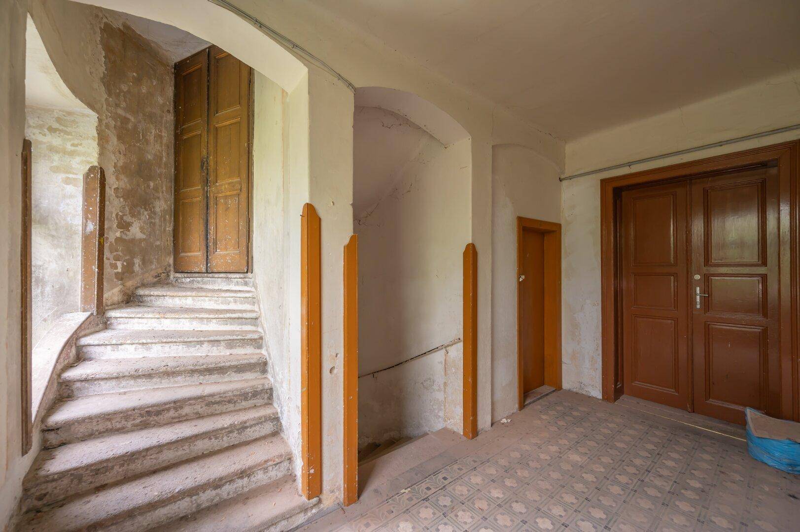 Eingangsbereich mit Steintreppe und Holztüren, der den Charme des Altbaus bewahrt und saniert werden muss.