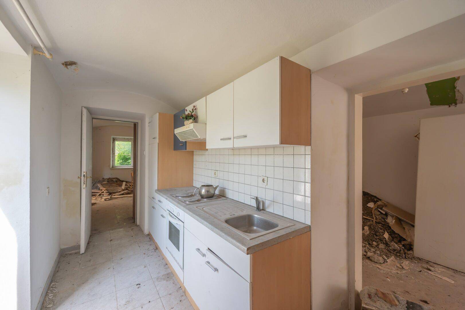 Renovierungsbedürftige Küche mit einfachen Schränken und Blick in weitere Räume.