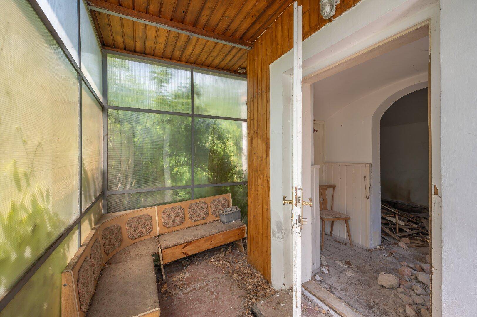 Verglaster Anbau mit Holzdecke und alter Sitzbank, der eine umfassende Sanierung benötigt.