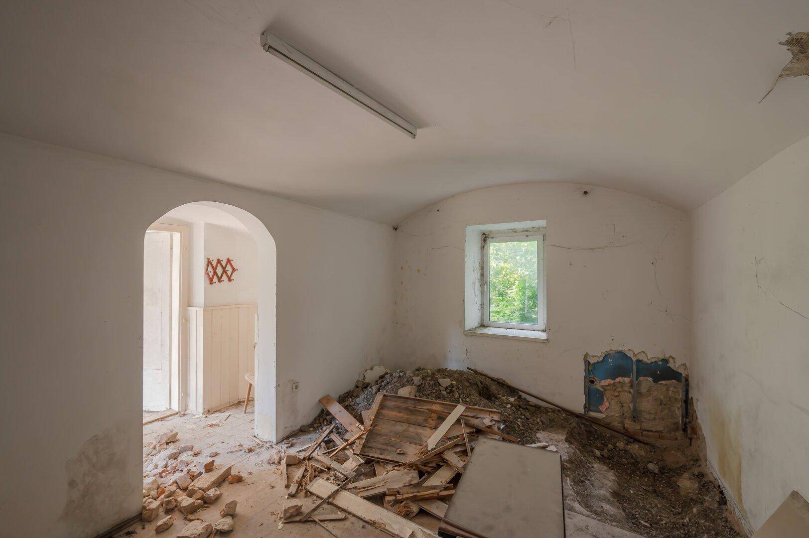 Leerer Raum mit Bauschutt und gewölbter Türöffnung, der auf eine Renovierung wartet.