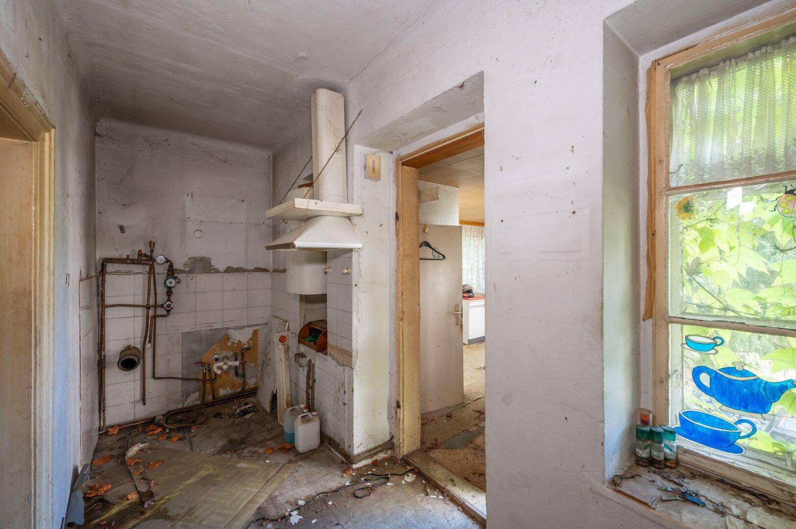 Leere Küche mit sichtbaren Rohren und Fliesen, die eine komplette Sanierung erfordert.