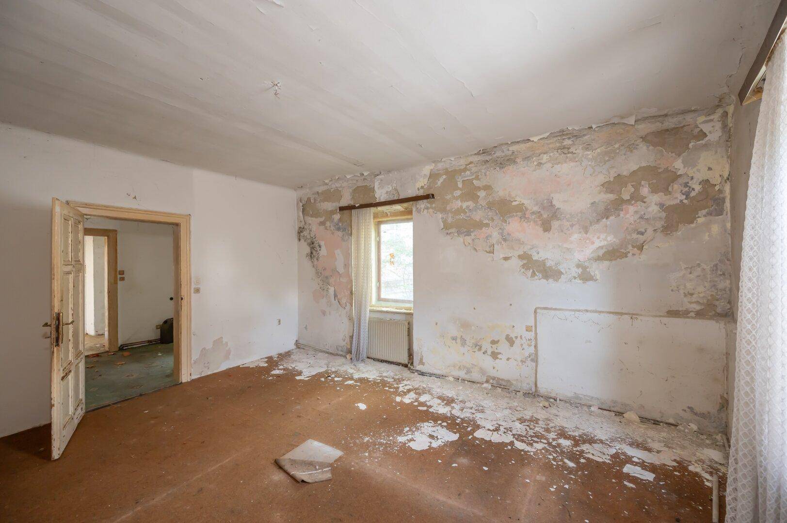 Renovierungsbedürftiges Zimmer mit abblätternden Wänden und Laminatboden, bereit zur Neugestaltung.