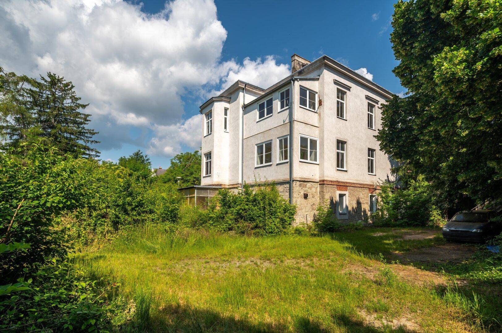 Historisches Gebäude mit großer Grünfläche und Bäumen, das eine umfassende Landschaftsgestaltung benötigt.