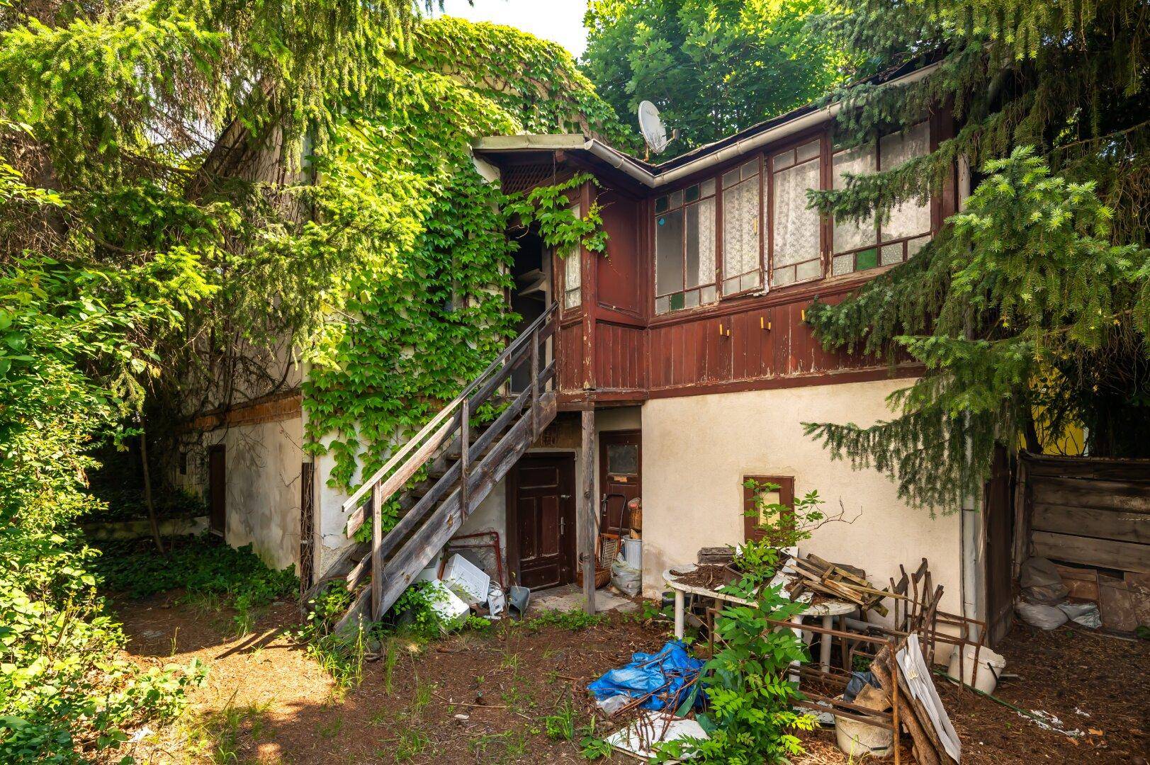 Rückseite eines alten Hauses mit Holzbalkon und üppigem Efeu an der Fassade.