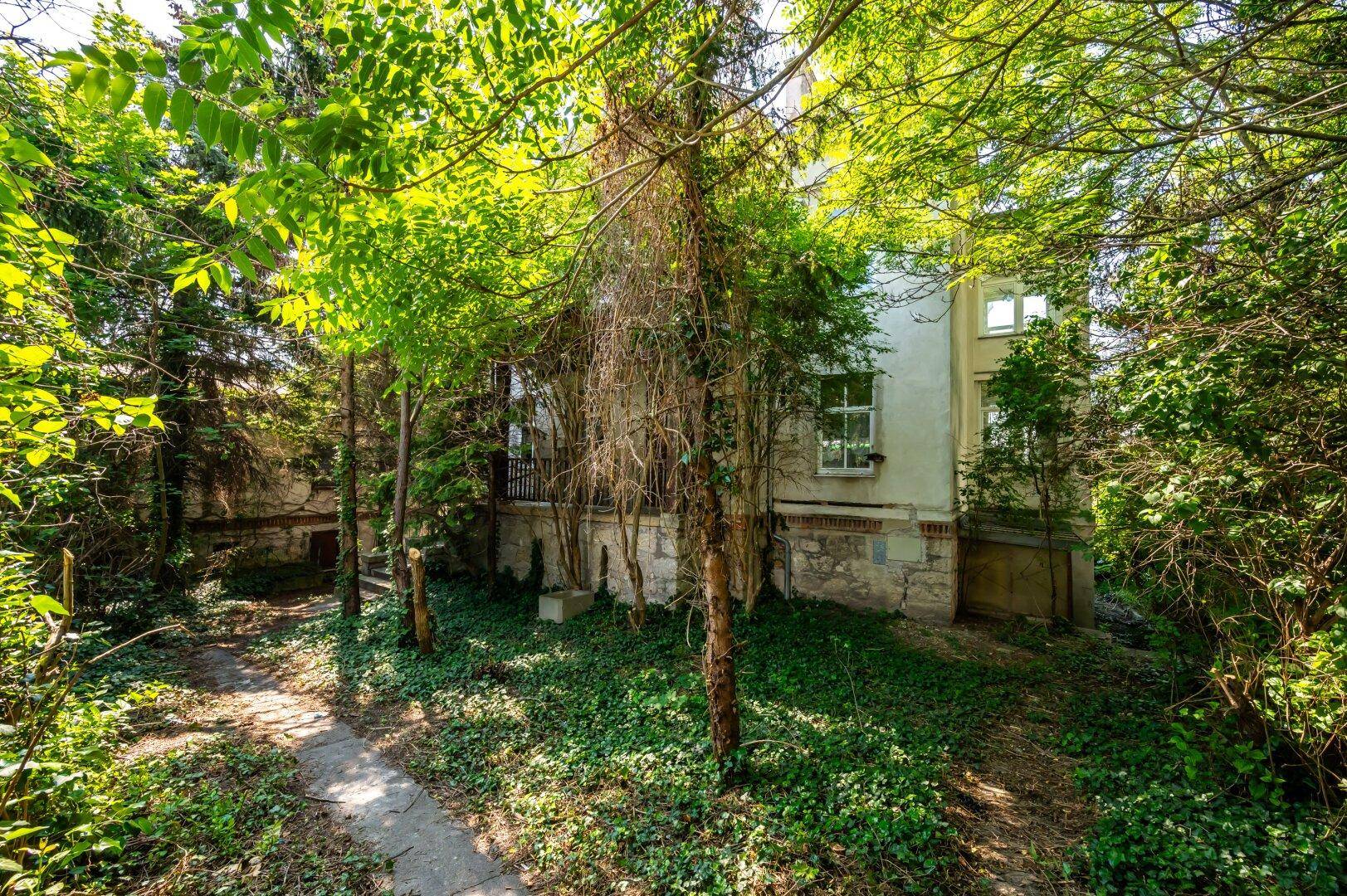 Altes Wohnhaus eingebettet in eine grüne Umgebung mit vielen Bäumen und Sträuchern.