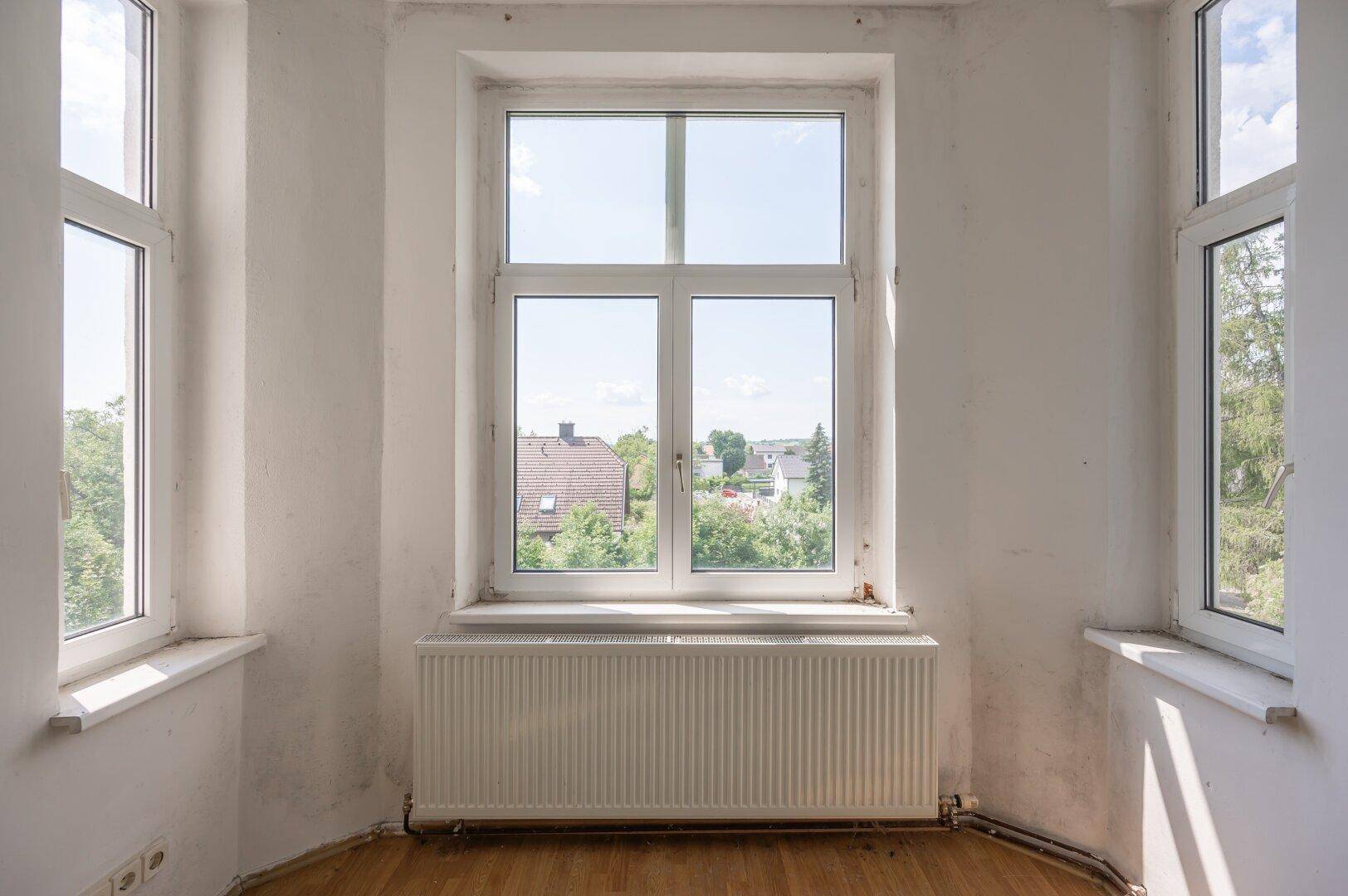 Heller Innenraum mit großen Fenstern, Heizkörper und Holzboden, bietet weite Aussicht.