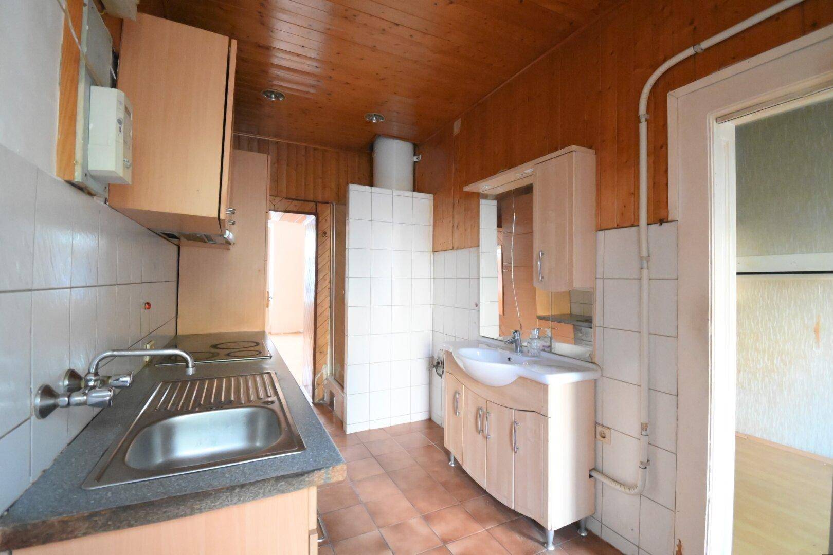 Funktionale Küche mit Holzdecke, Fliesenboden und integrierter Spüle sowie Kochfeld.