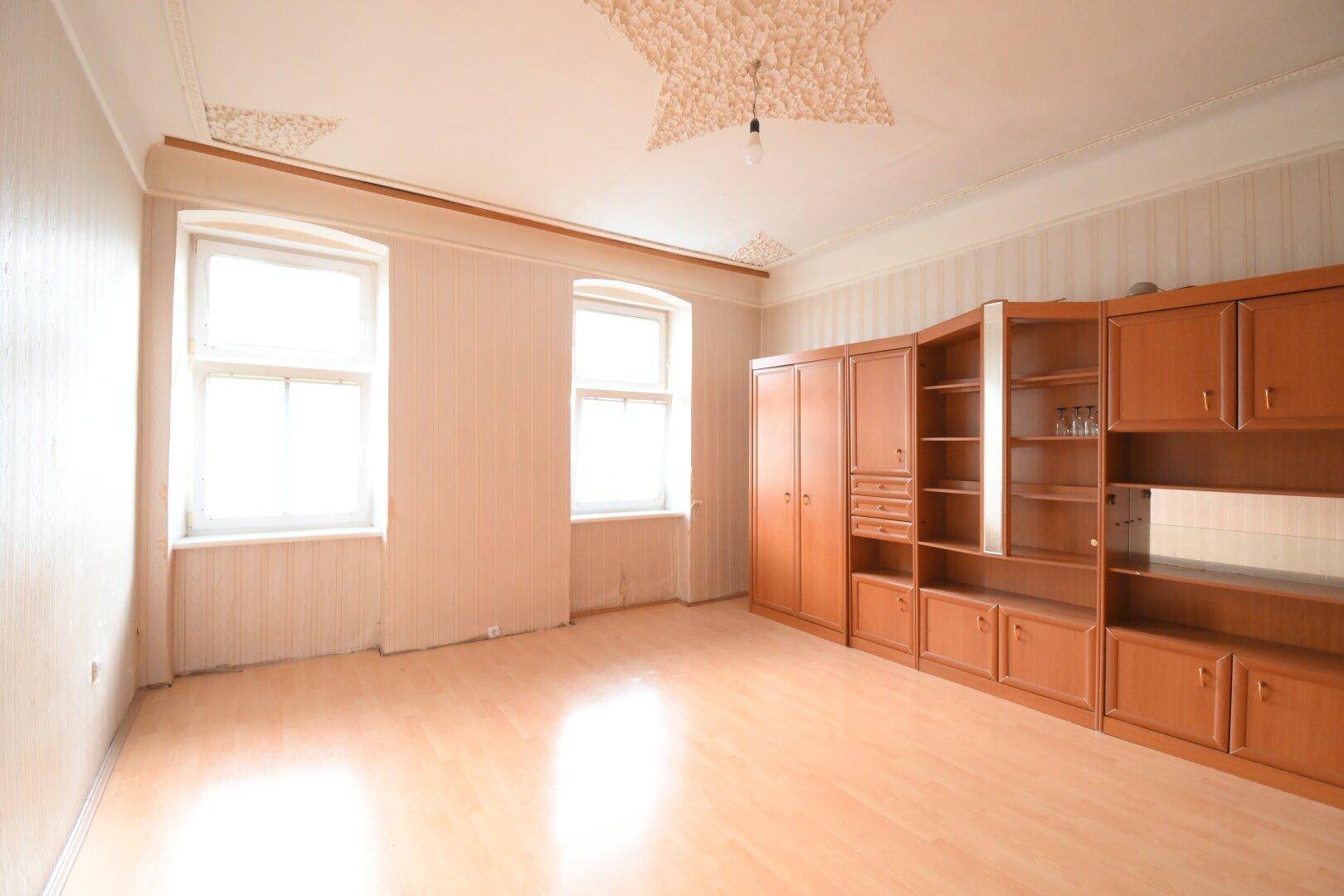 Helles Zimmer mit Laminatboden, zwei Fenstern und einer umfangreichen Holzschrankwand.