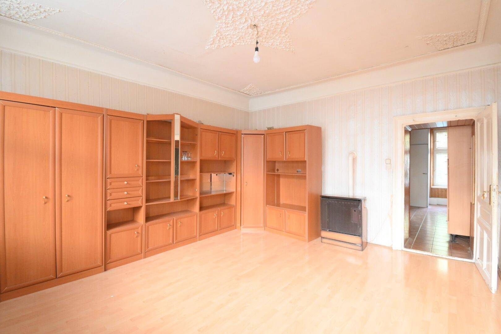 Großes Zimmer mit Laminatboden, Stuckdecke und einer umfangreichen Holzschrankwand sowie Ofen.