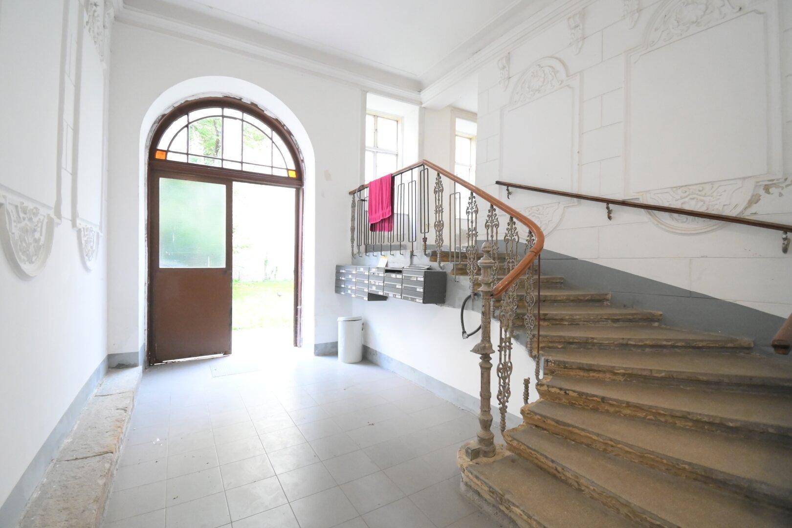 Historisches Treppenhaus mit geschwungenem Geländer, hohen Decken und dekorativen Elementen.