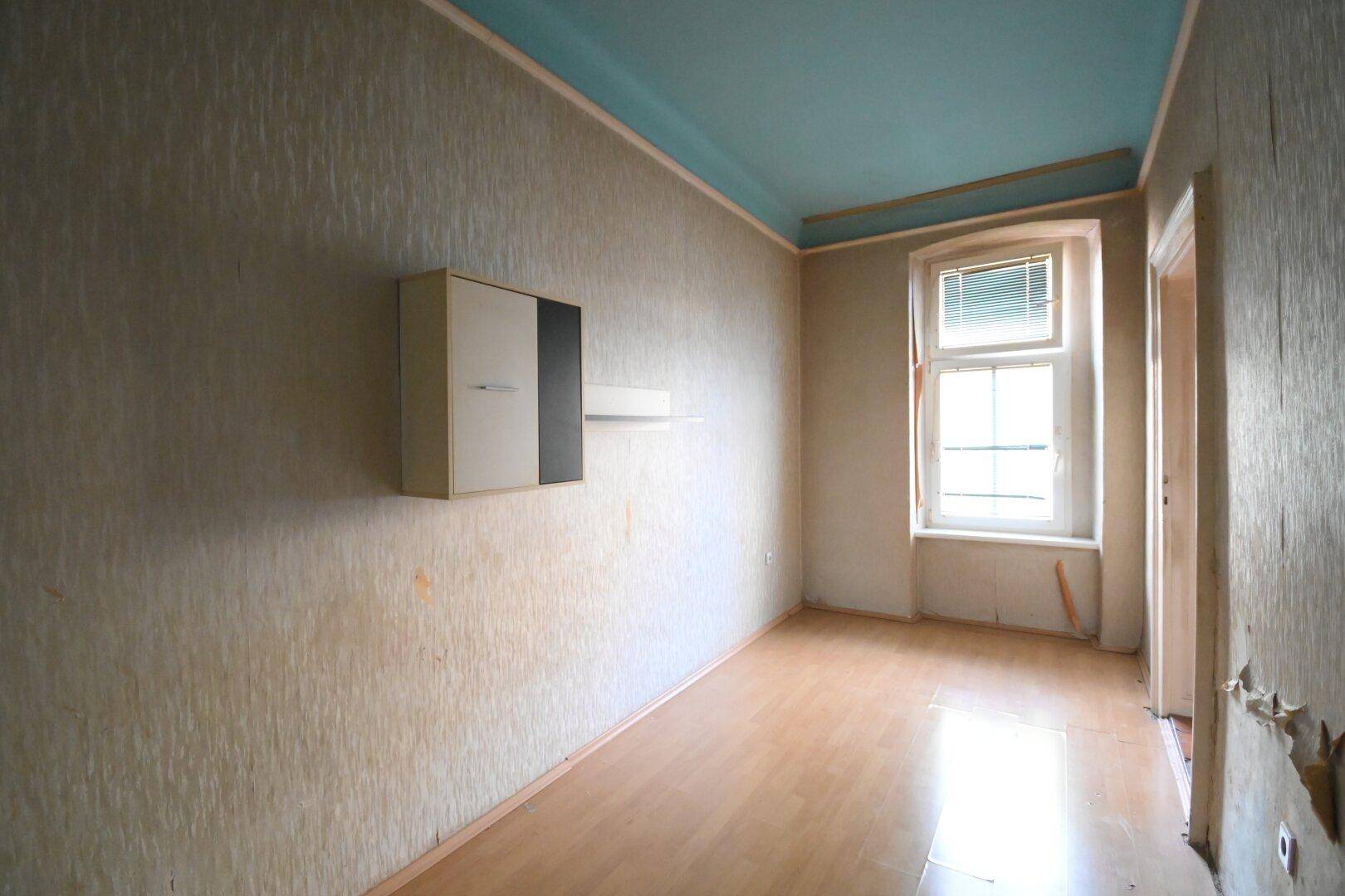 Helles Zimmer mit Laminatboden, einem Fenster und einer blauen Decke, bereit zur Gestaltung.