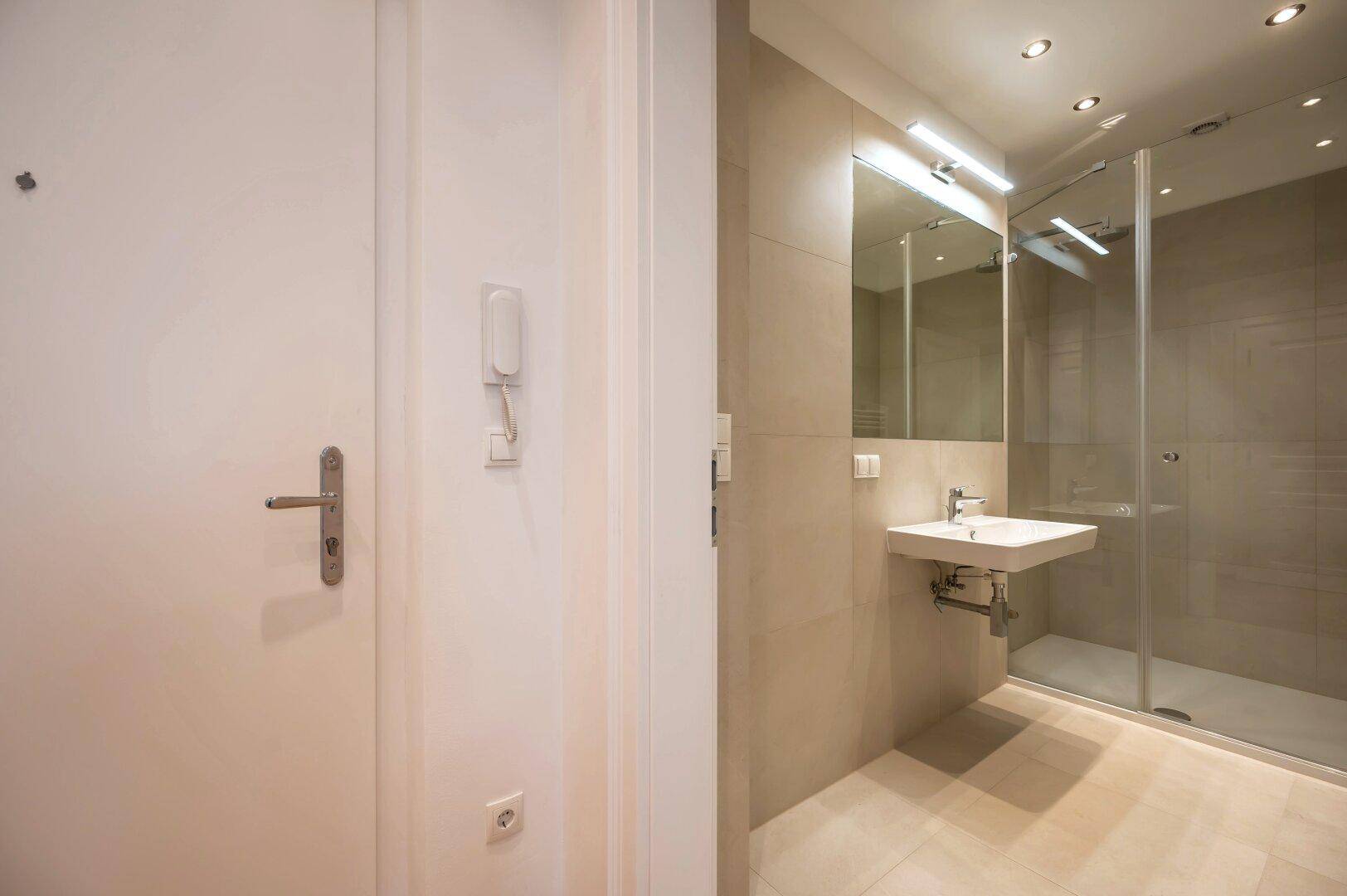Modernes Badezimmer mit beigefarbenen Fliesen, Waschbecken und einer geräumigen Glasdusche.
