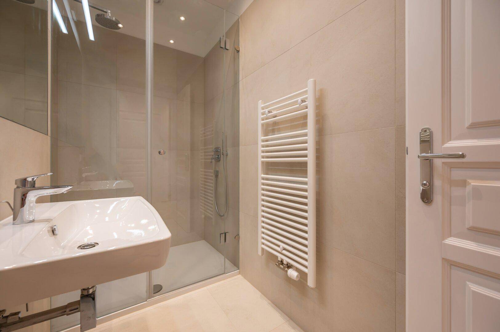 Detaillierte Ansicht des modernen Badezimmers mit Waschbecken, Handtuchheizkörper und Regendusche.