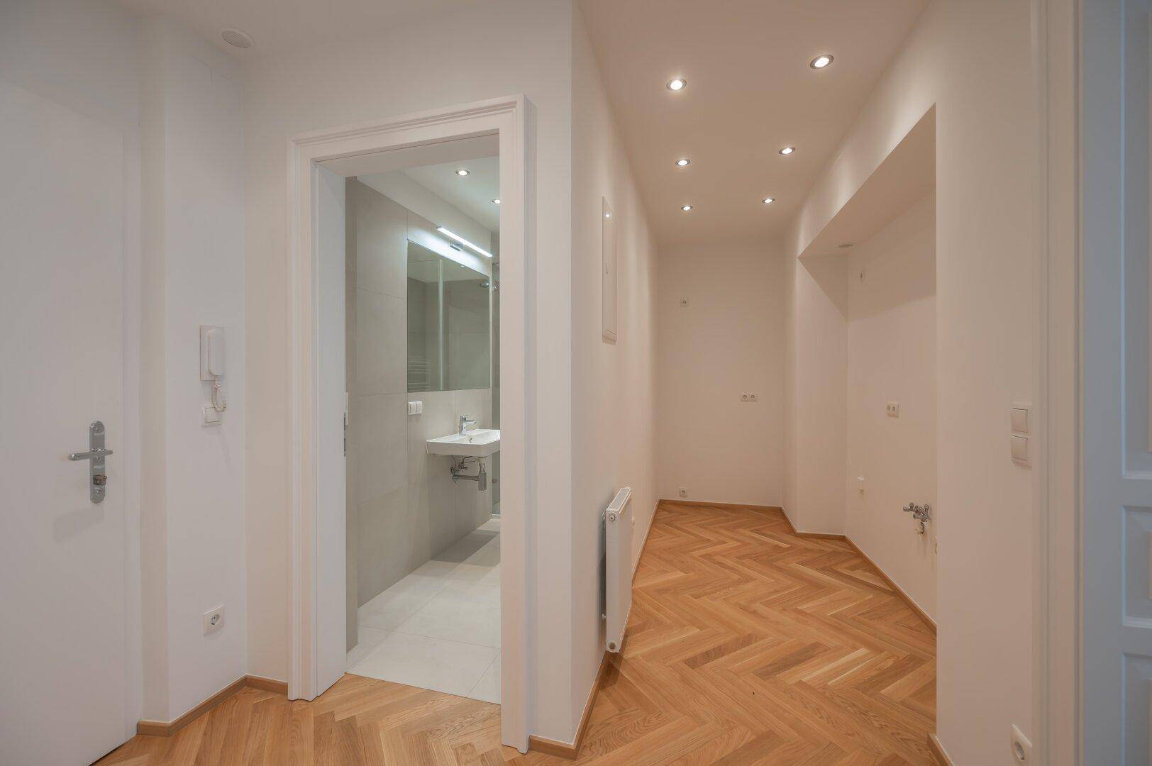 Geräumiger Flur mit Fischgrätparkett, Einbaustrahlern und Zugang zum modernen Badezimmer.