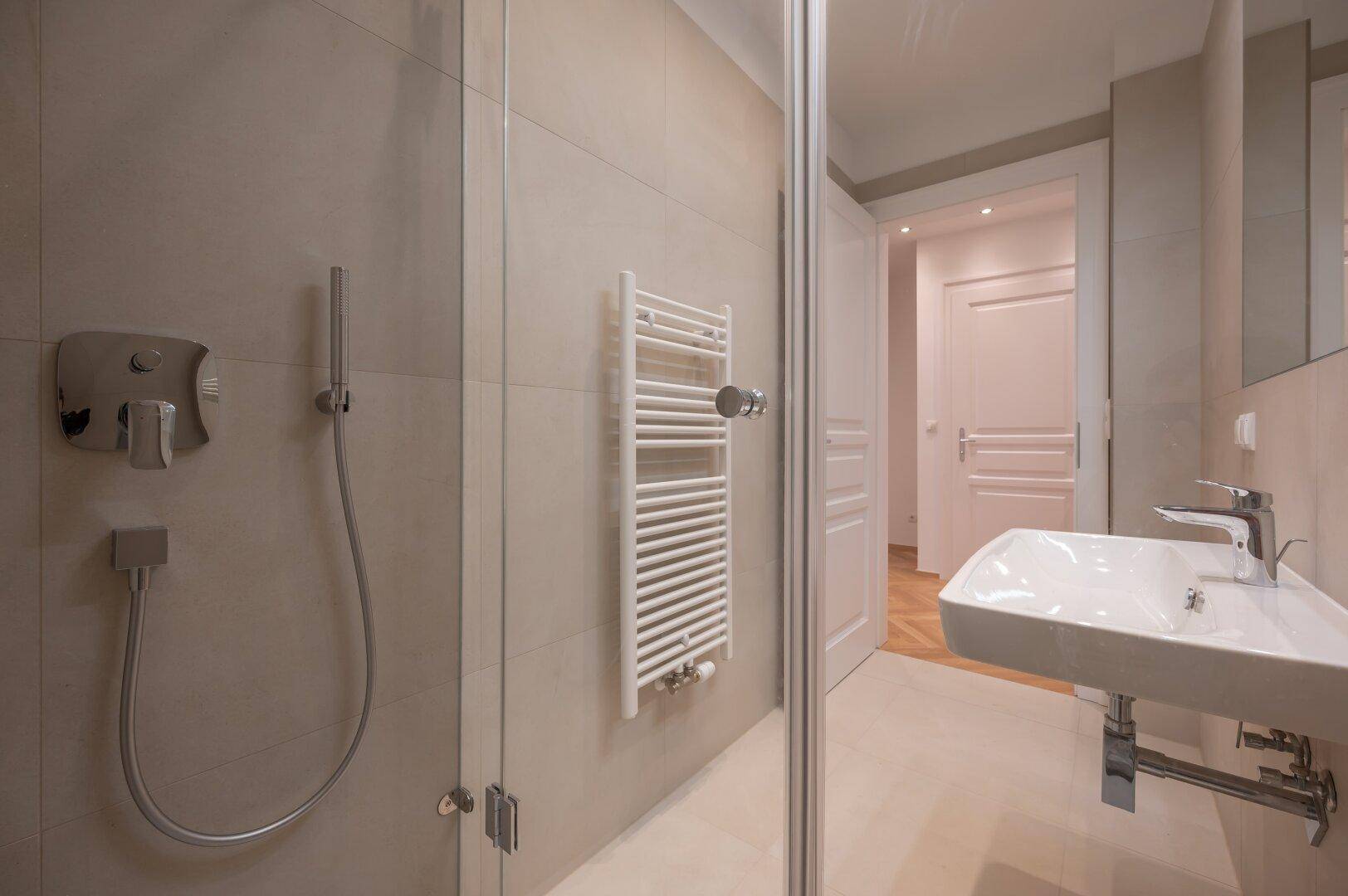 Badezimmer mit Glasdusche und modernem Waschbecken, verbunden mit dem hellen Flur.