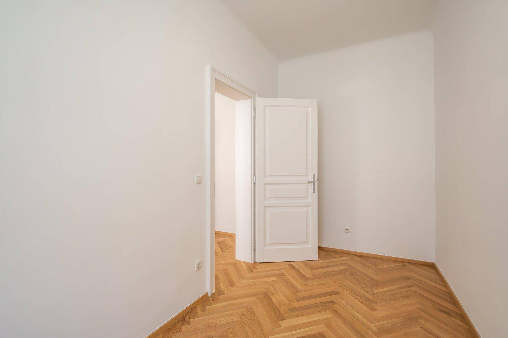 Leerer Raum mit klassischem Fischgrätparkett und weiß gestrichenen Wänden, vielseitig nutzbar.