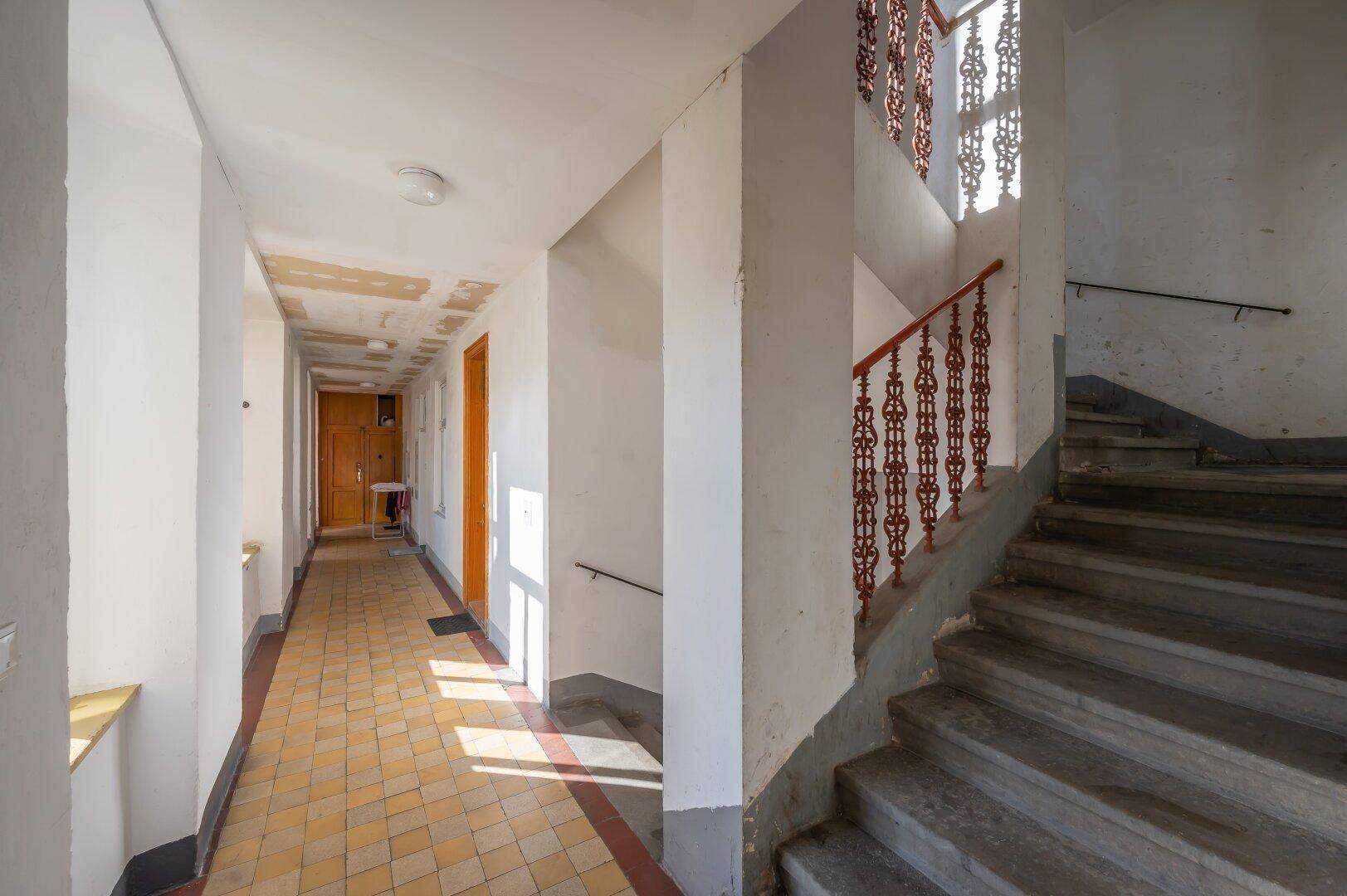 Treppenhaus in einem Altbau mit gefliestem Flur und historischem Geländer.