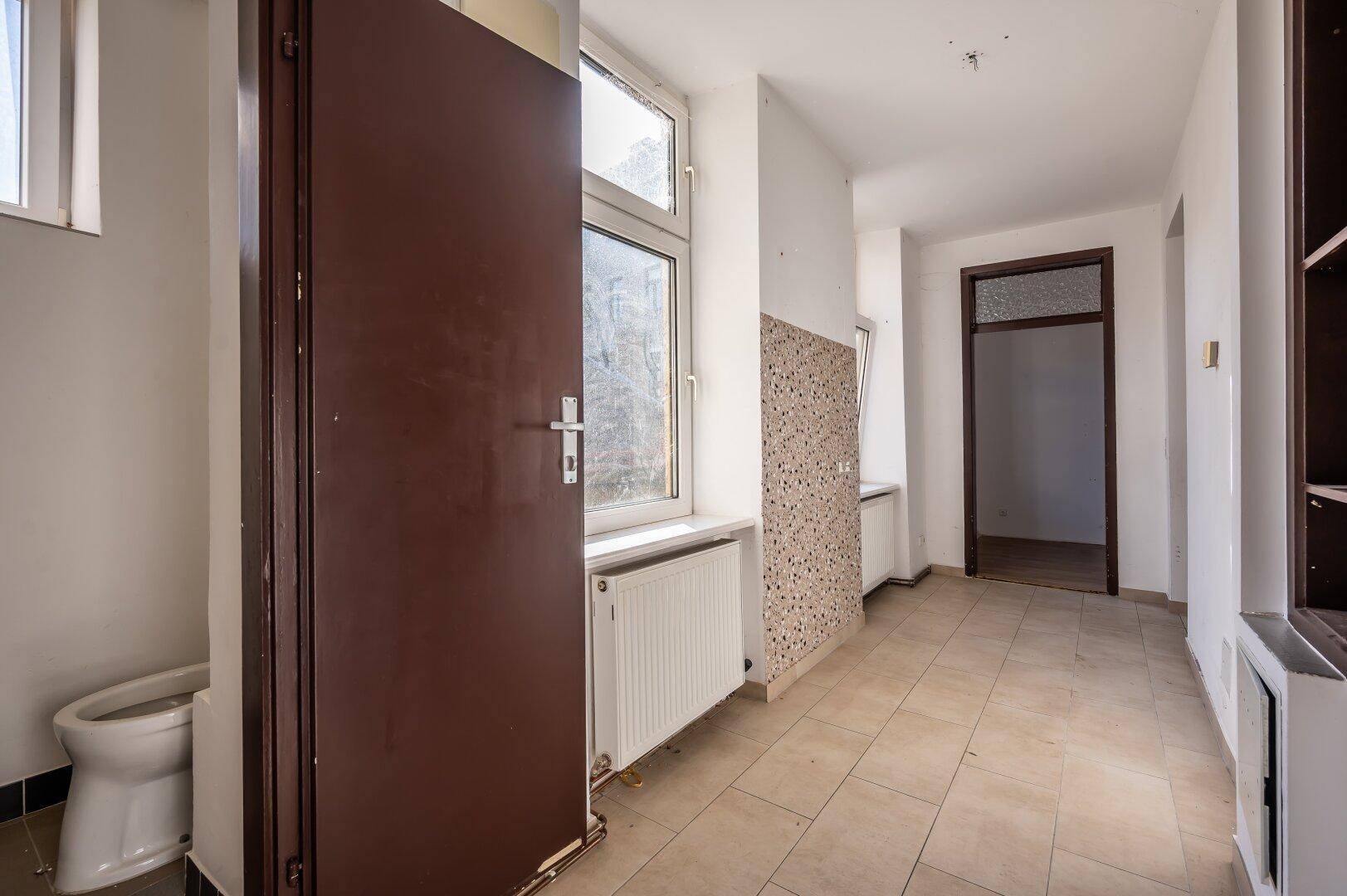 Flur mit Fliesenboden und Fenster, angrenzend an einen Sanitärbereich.