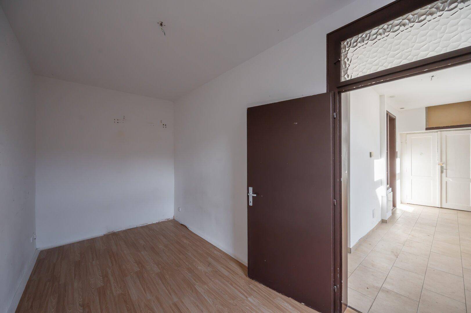 Leerer Raum mit Holzboden und geschlossener Tür, angrenzend an einen weiteren Bereich.