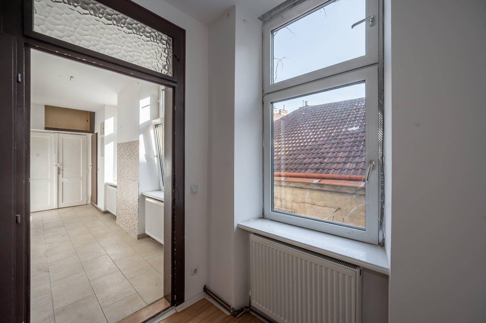 Flur mit Fliesenboden und Fenster, das einen Blick auf die Dächer bietet.