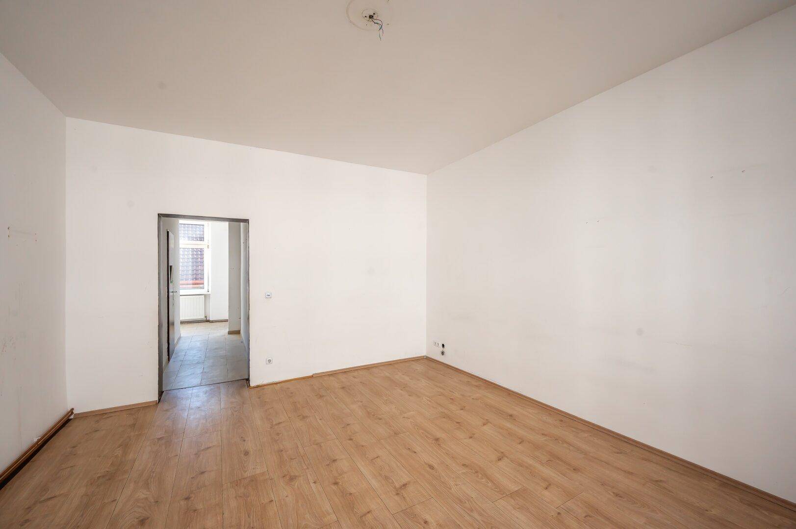 Leerer Raum mit Holzboden und offenem Durchgang zu einem weiteren Zimmer.