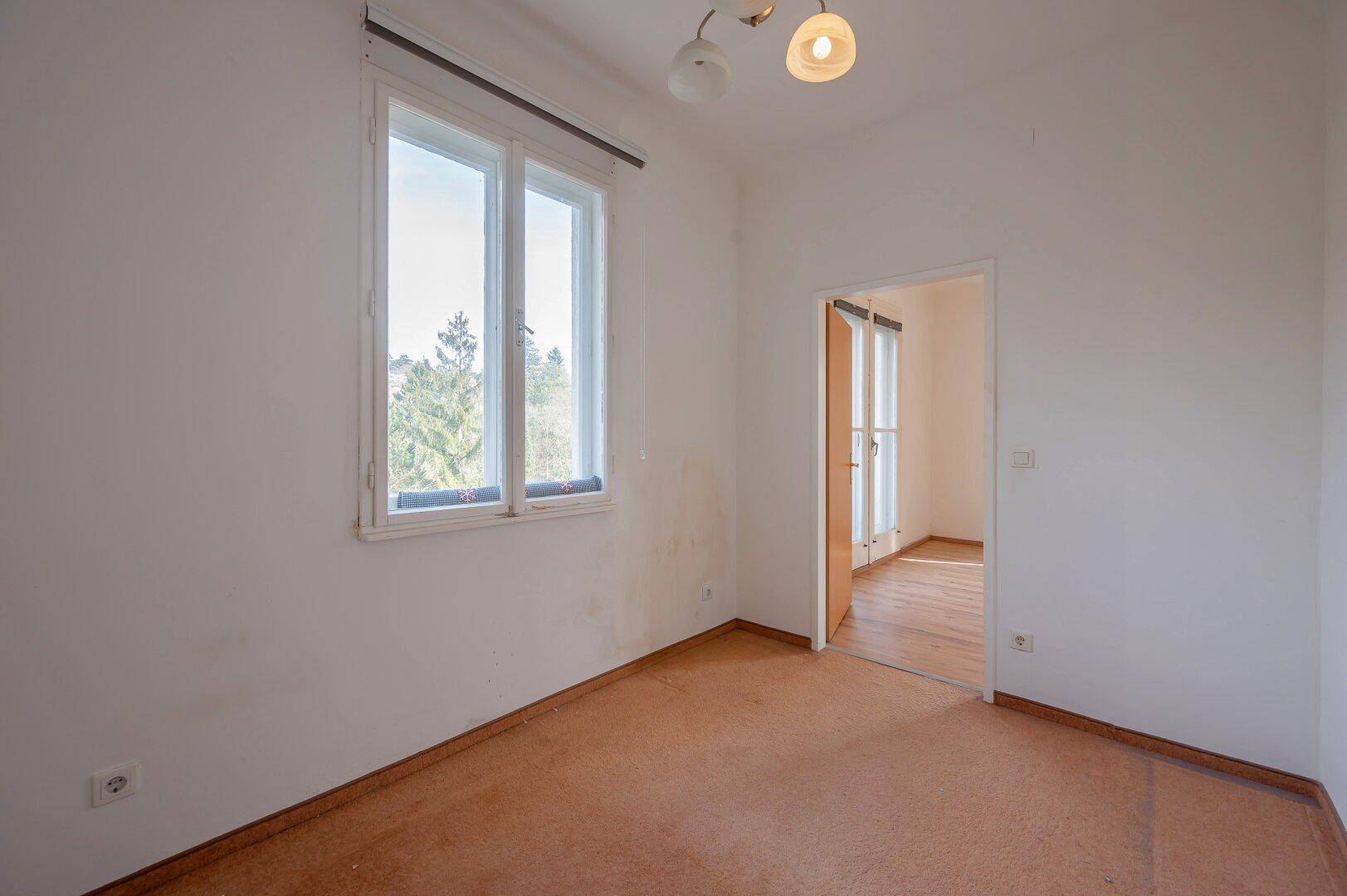Schlafzimmer mit Teppichboden und einem großen Fenster, das viel Tageslicht hereinlässt.