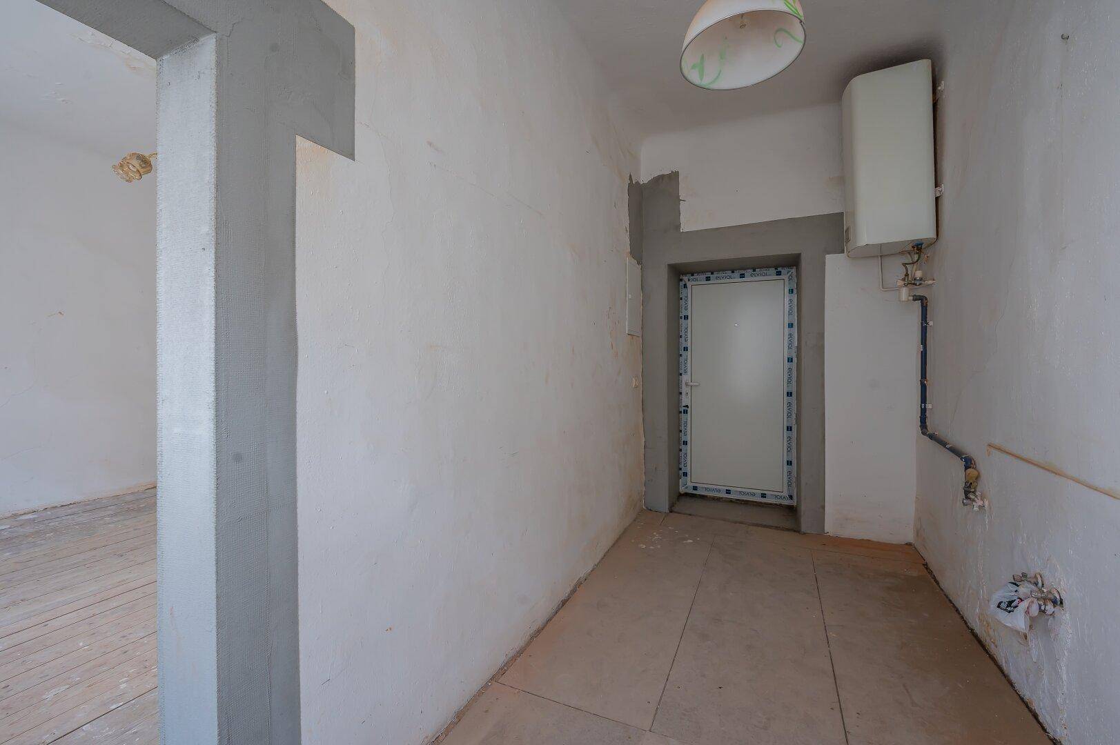 Kleiner Raum in Renovierungszustand mit Fliesenboden, Warmwasserbereiter und sichtbaren Leitungen.