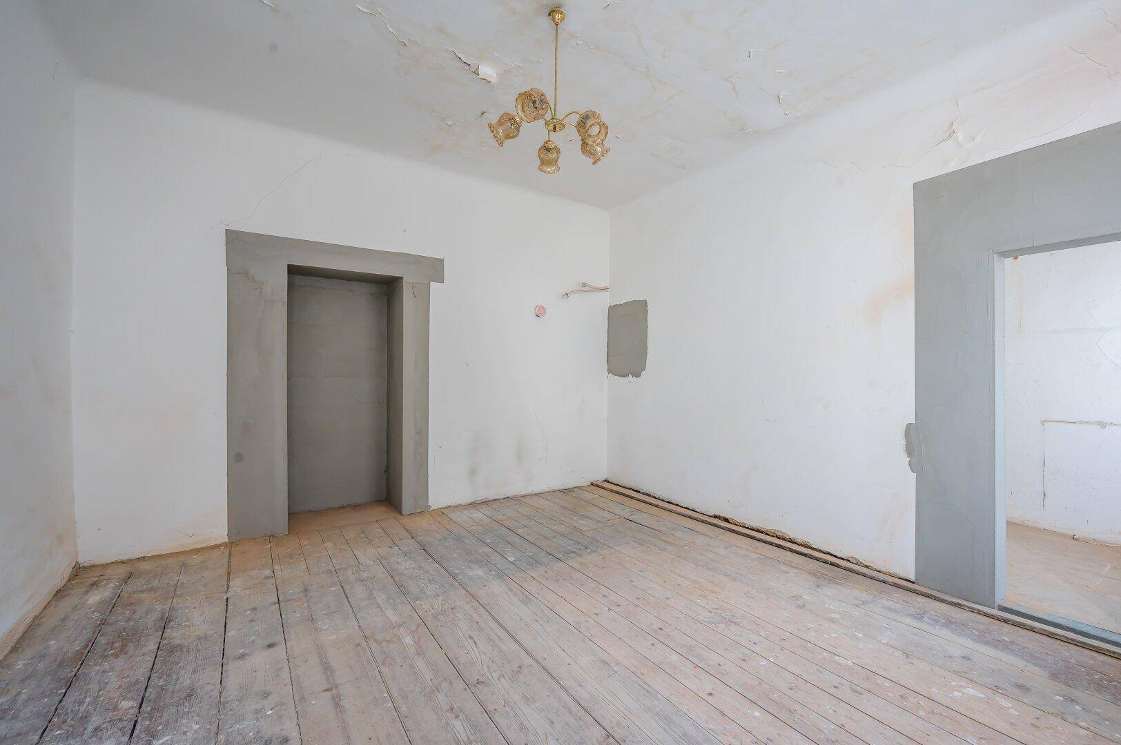 Leerer Raum in Sanierungszustand mit alten Holzdielen und unfertigen Wänden, bereit für die Renovierung.
