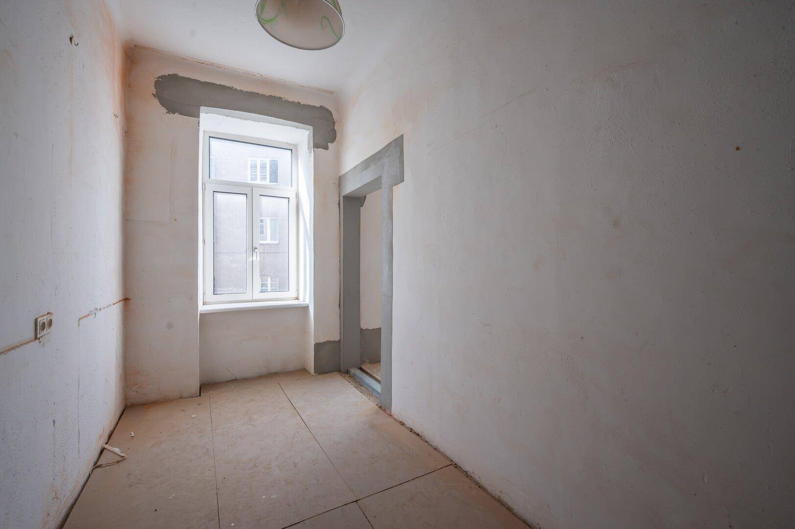 Kleiner Raum in Renovierungszustand mit Fliesenboden und einem Fenster, ideal für einen Flur.