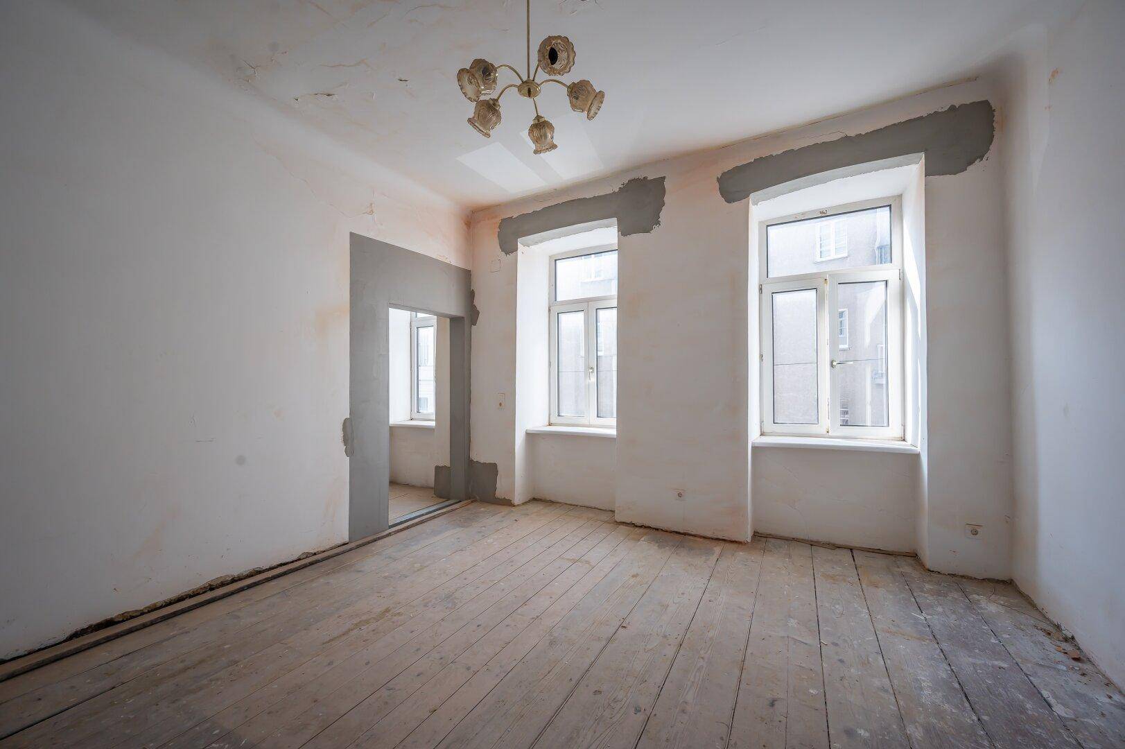 Unmöblierter Raum in Renovierungszustand mit alten Holzdielen und abgeblätterter Decke, bereit zur Sanierung.
