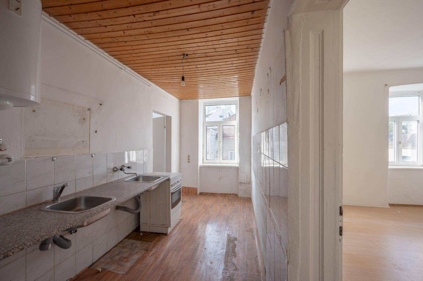 Unsanierte Küche mit Holzdecke, Spülbecken und Herd, die auf eine Modernisierung wartet.