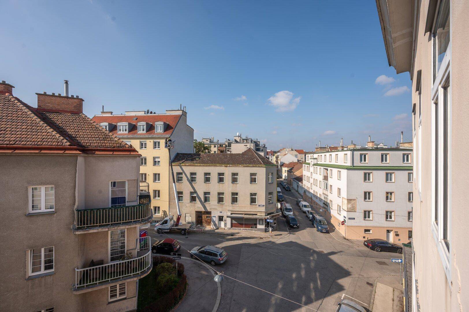 Blick von oben auf eine belebte Stadtstraße mit parkenden Autos und umliegenden Gebäuden.