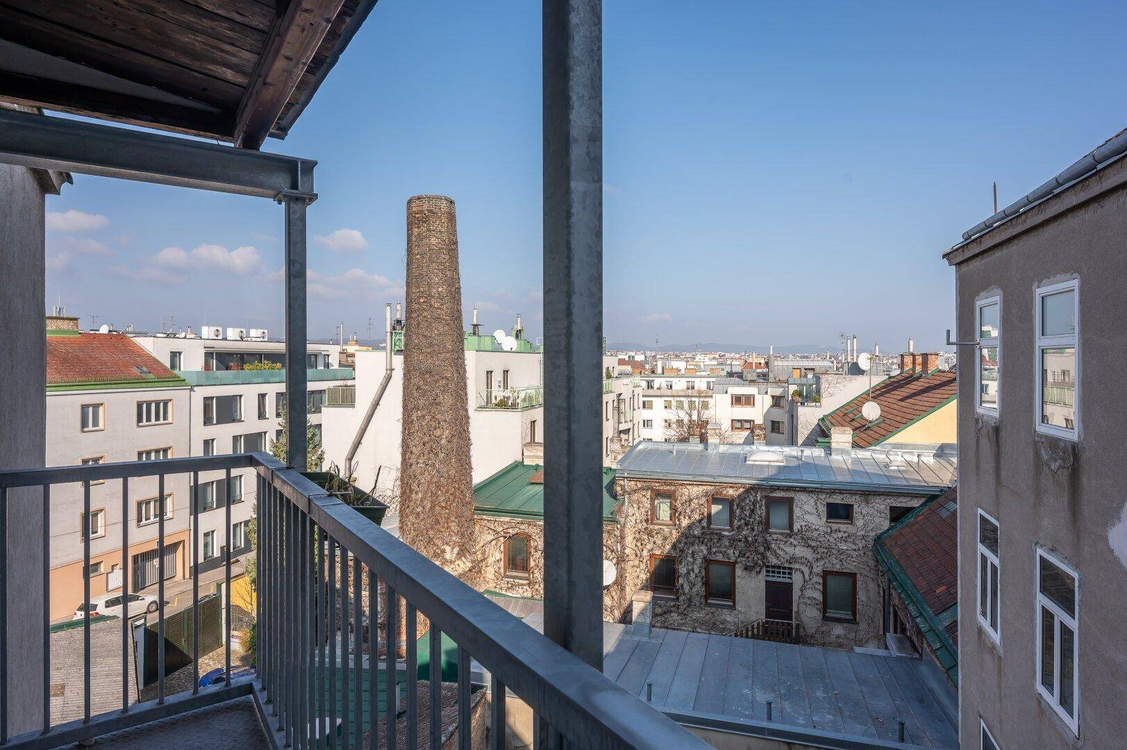 Balkon mit weitem Blick über die Dächer der Stadt und einen markanten Schornstein.