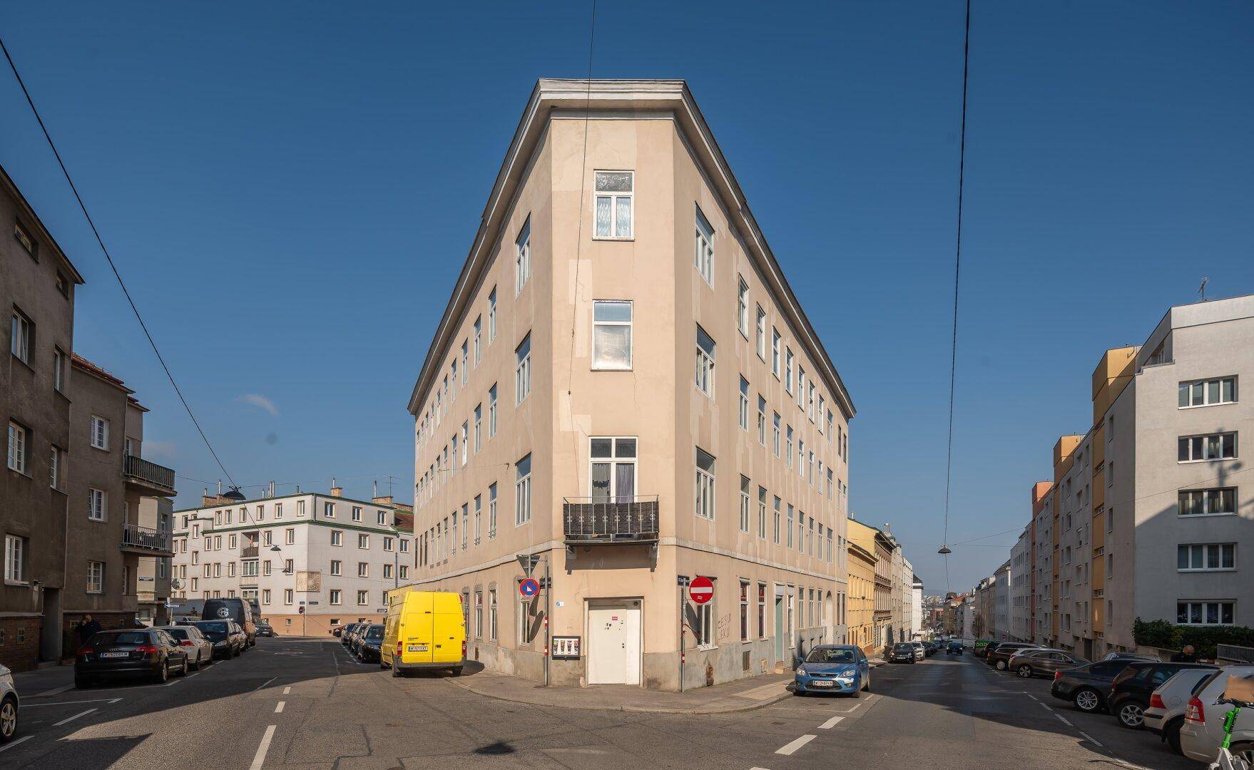 Eckgebäude an einer städtischen Kreuzung mit klassischer Architektur und vielen Fenstern.