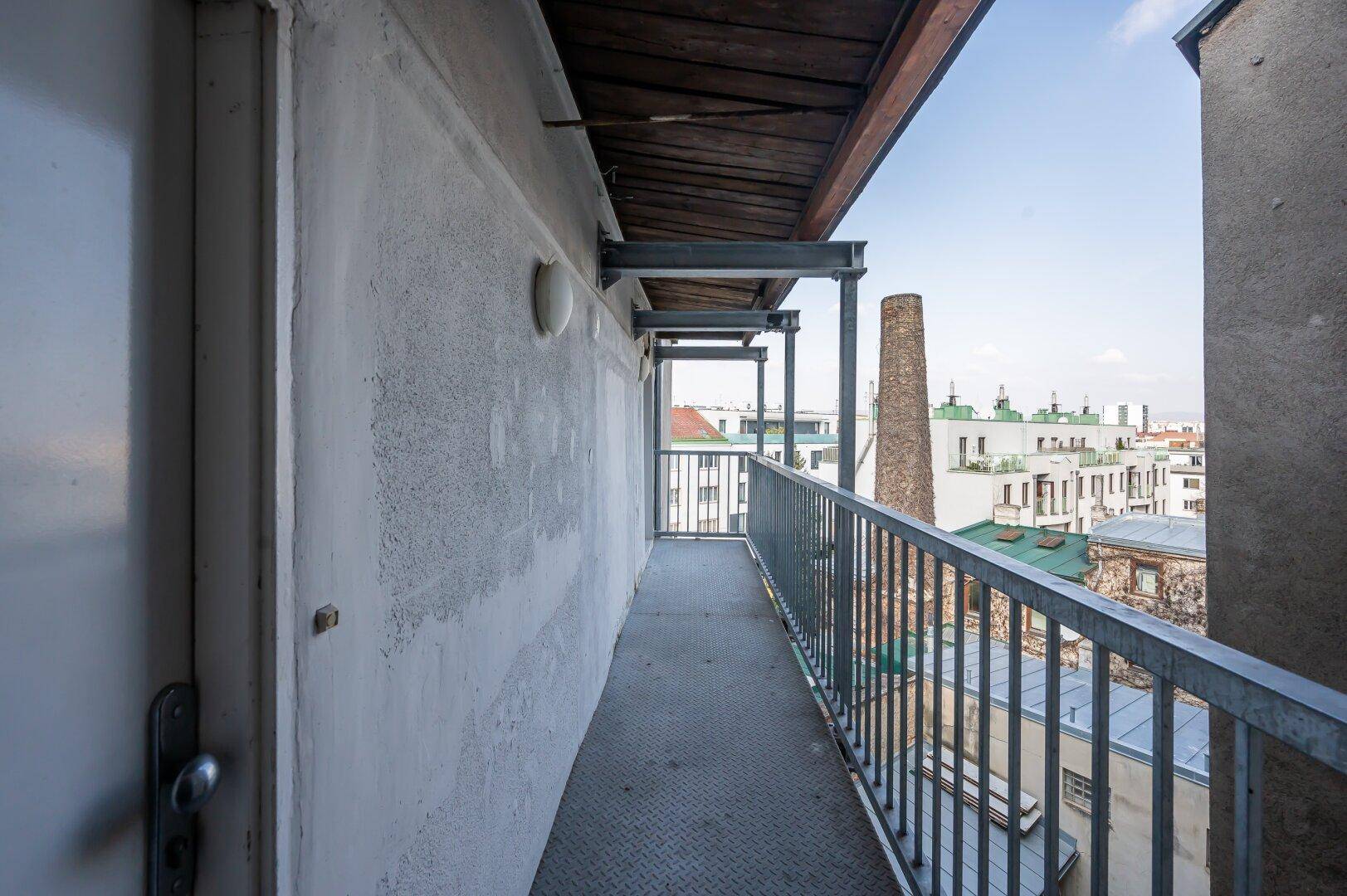 Langer Balkon mit Metallgeländer und Ausblick auf die städtische Umgebung und Dächer.