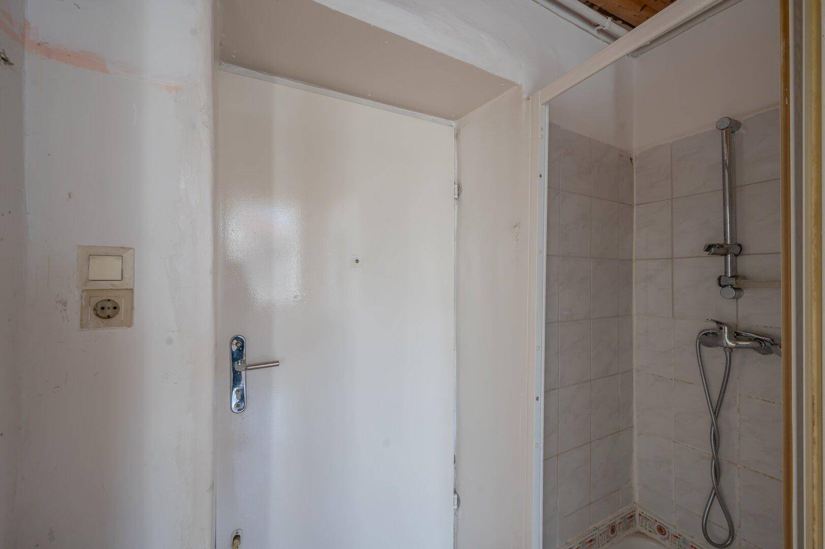 Badezimmer mit Duschkabine und gefliesten Wänden, das eine Modernisierung benötigt.